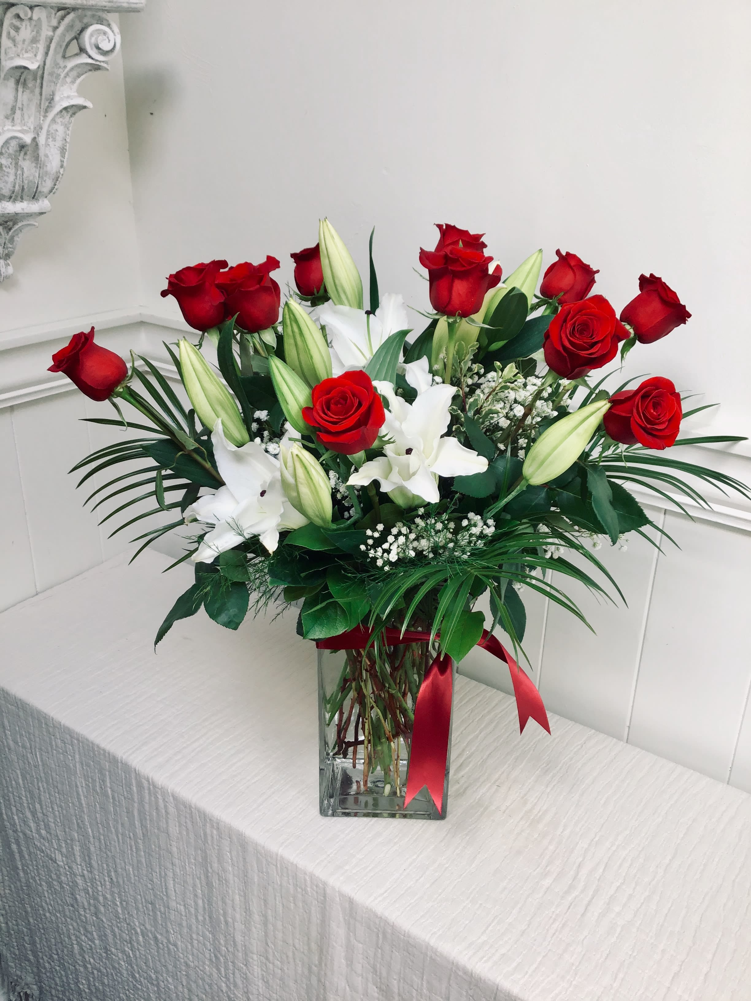 Red roses and white lilies in a clear glass vase with a red ribbon