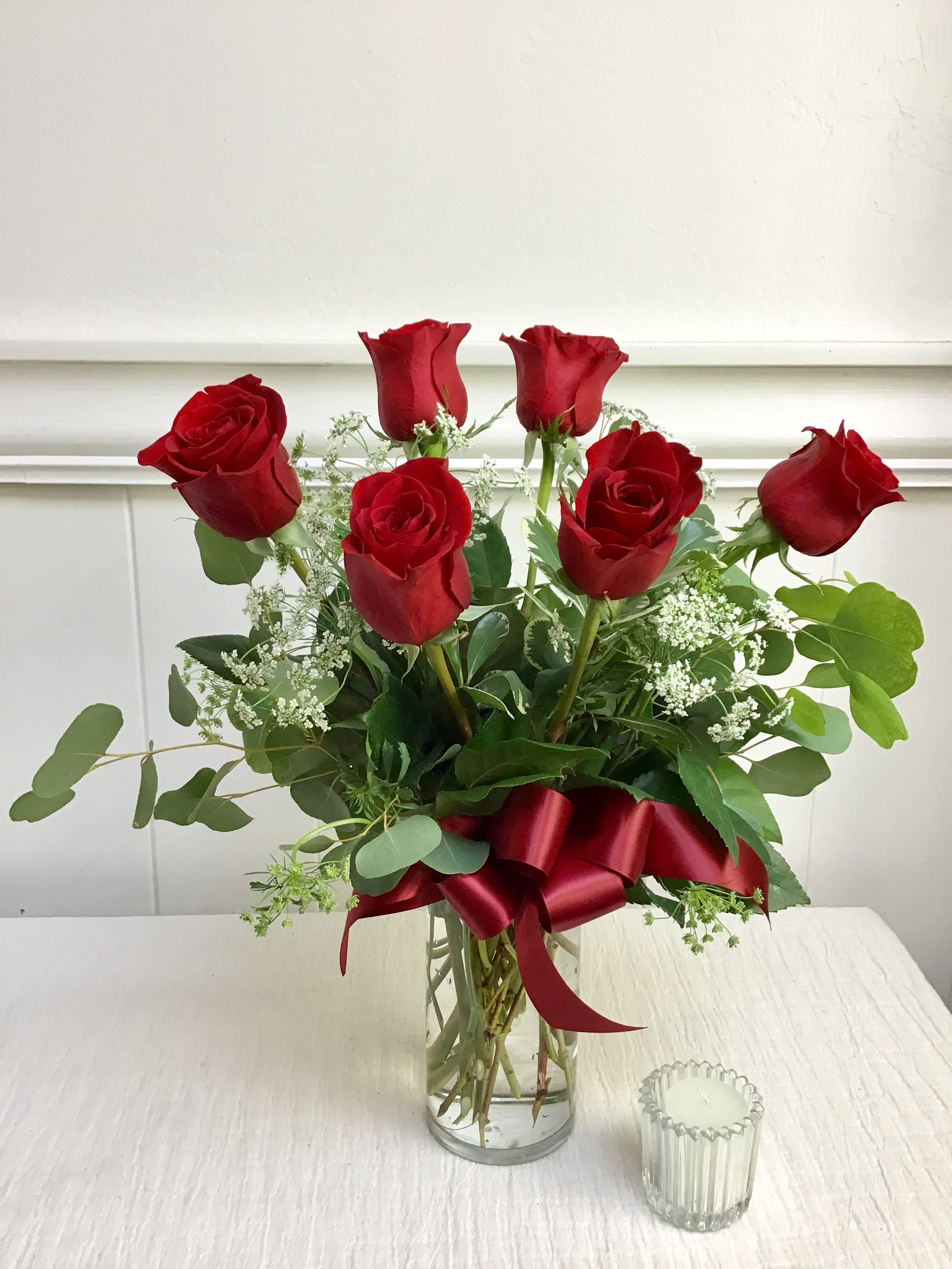 Red roses arranged in a clear glass vase with a red ribbon