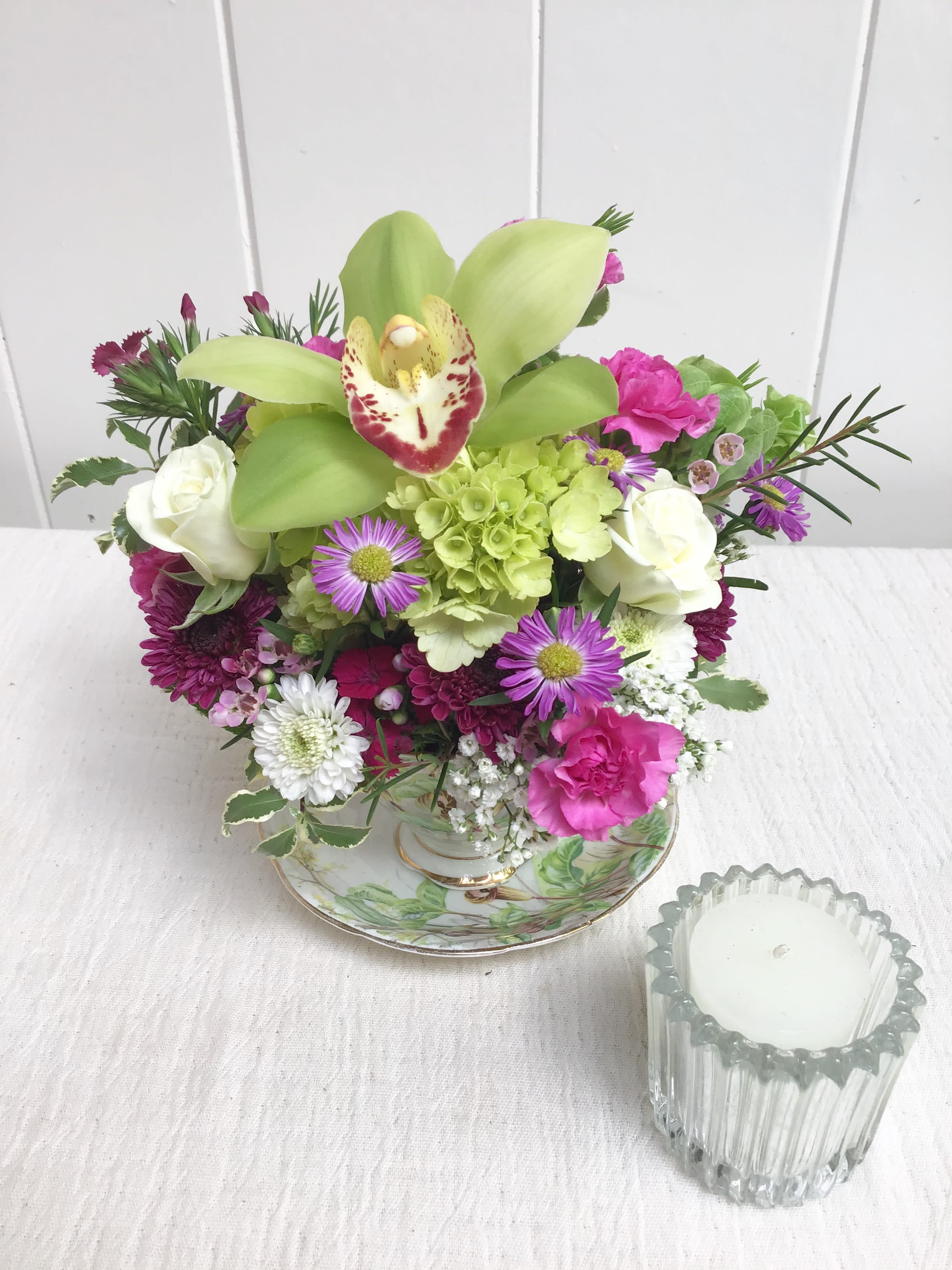 Mixed bouquet with green orchids, white roses, and pink flowers in a teacup-style vase