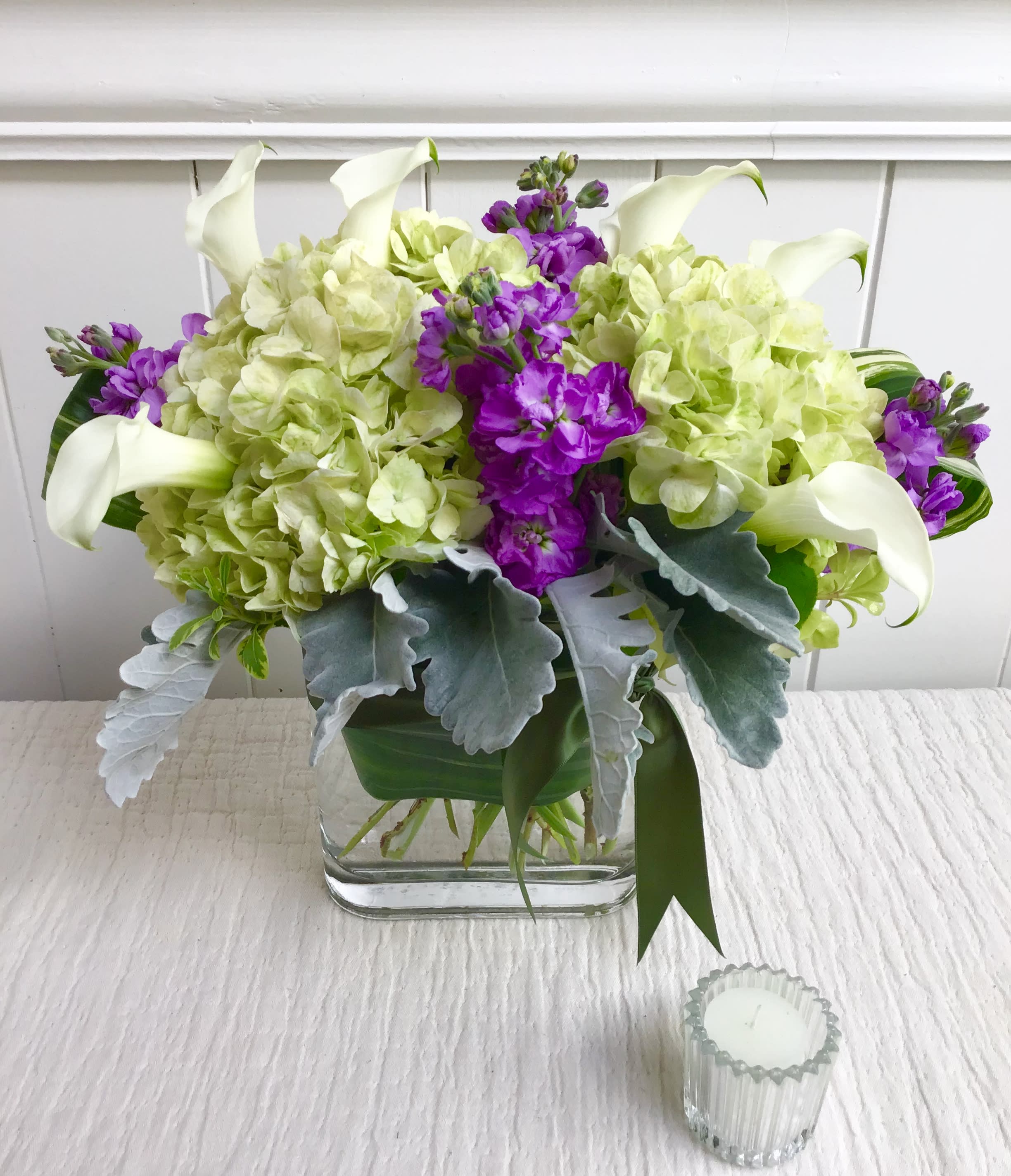 Arrangement of green hydrangeas, purple stock, and white calla lilies in a glass vase