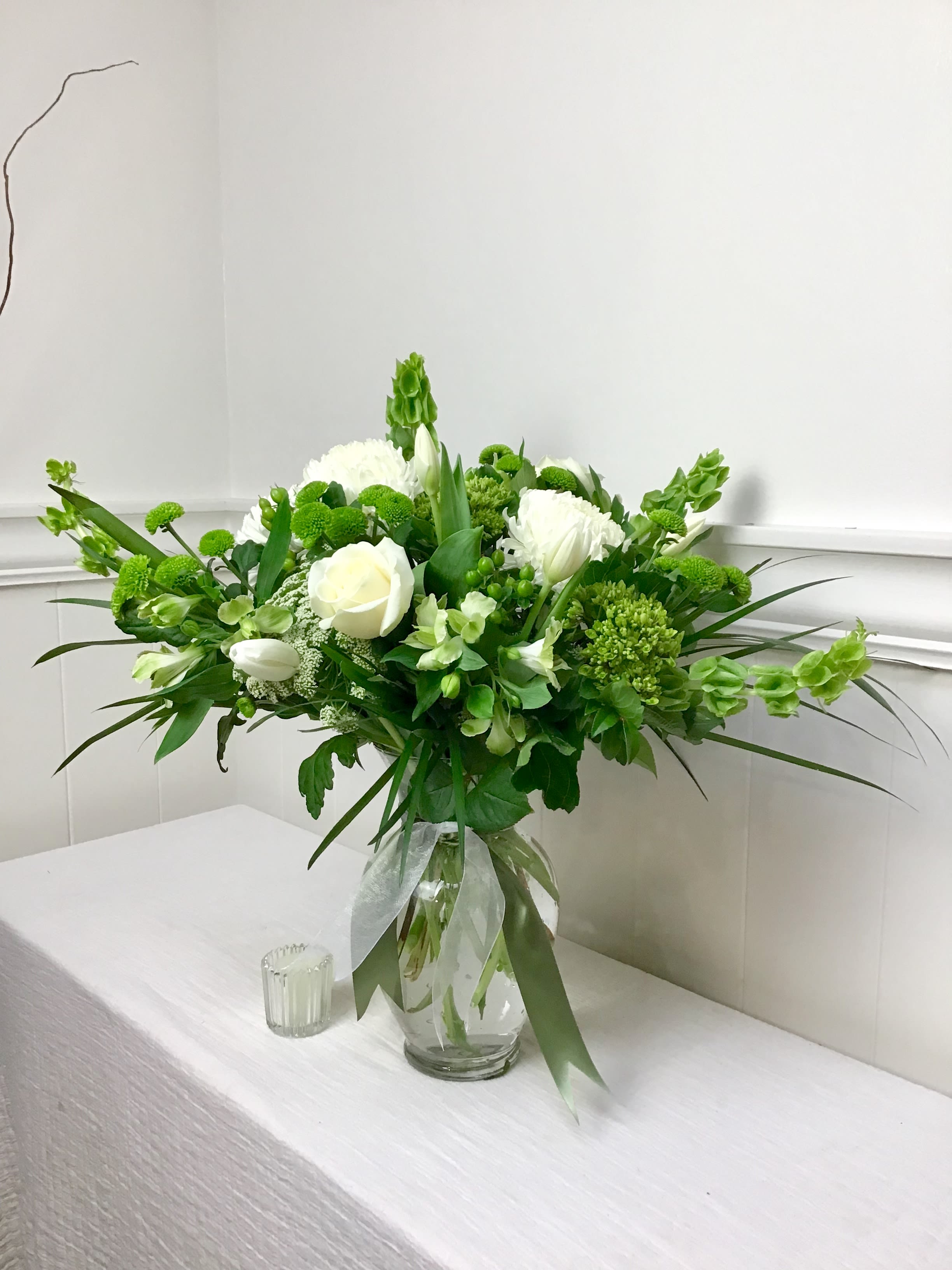 White and green floral arrangement in a glass vase with a ribbon