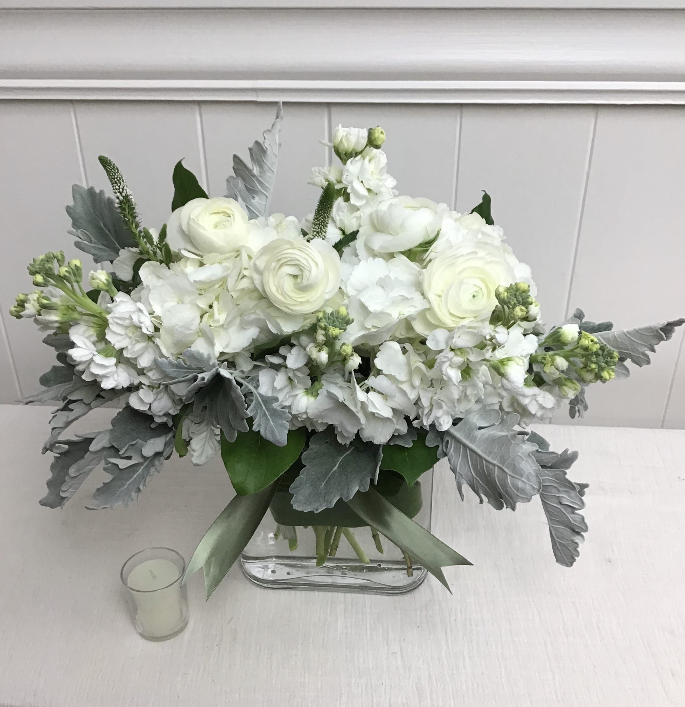 White floral arrangement in a clear rectangular vase with silver foliage