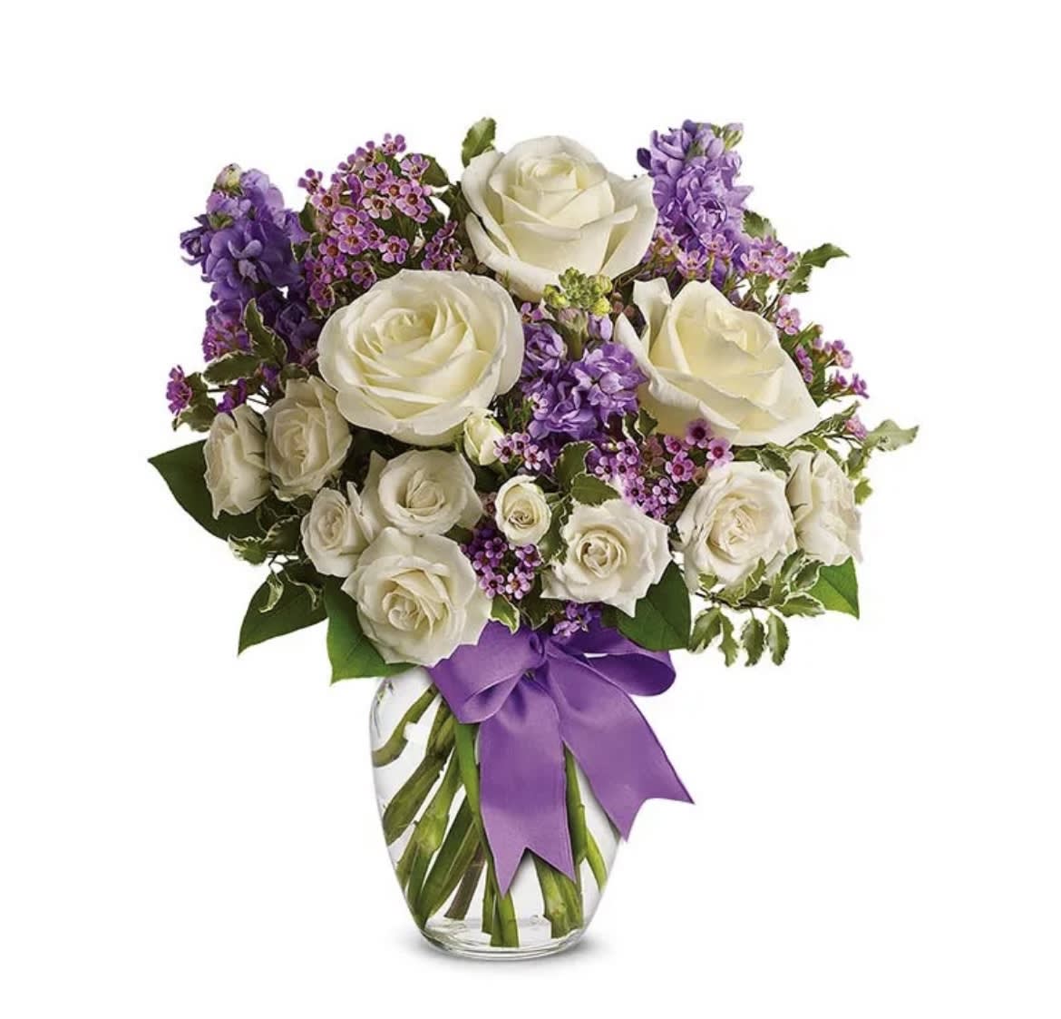 White roses and purple flowers in a clear glass vase with a purple ribbon