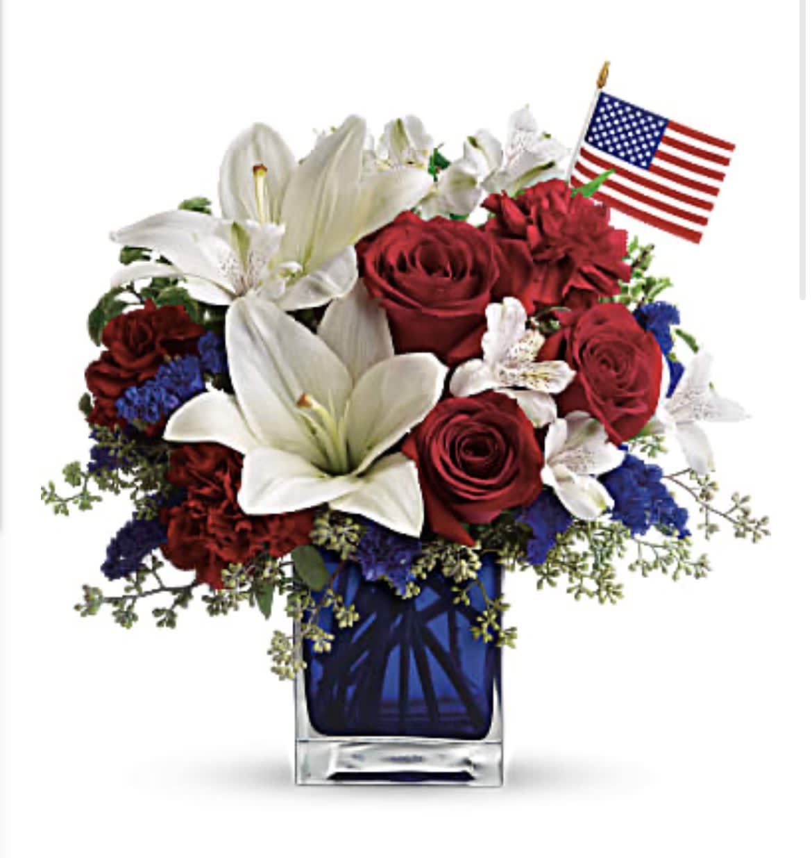 America The Beautiful - A patriotic pick to send a brave veteran, decorate your Fourth of July picnic, or celebrate Memorial Day. Lush red, white and blue flowers are presented in a deep blue glass cube vase along with an American flag. Red roses, white asiatic lilies, white alstroemeria, blue statice and red carnations are gathered with green pitta negra, seeded eucalyptus and a small American flag in a cobalt blue glass cube. Orientation: All-Around