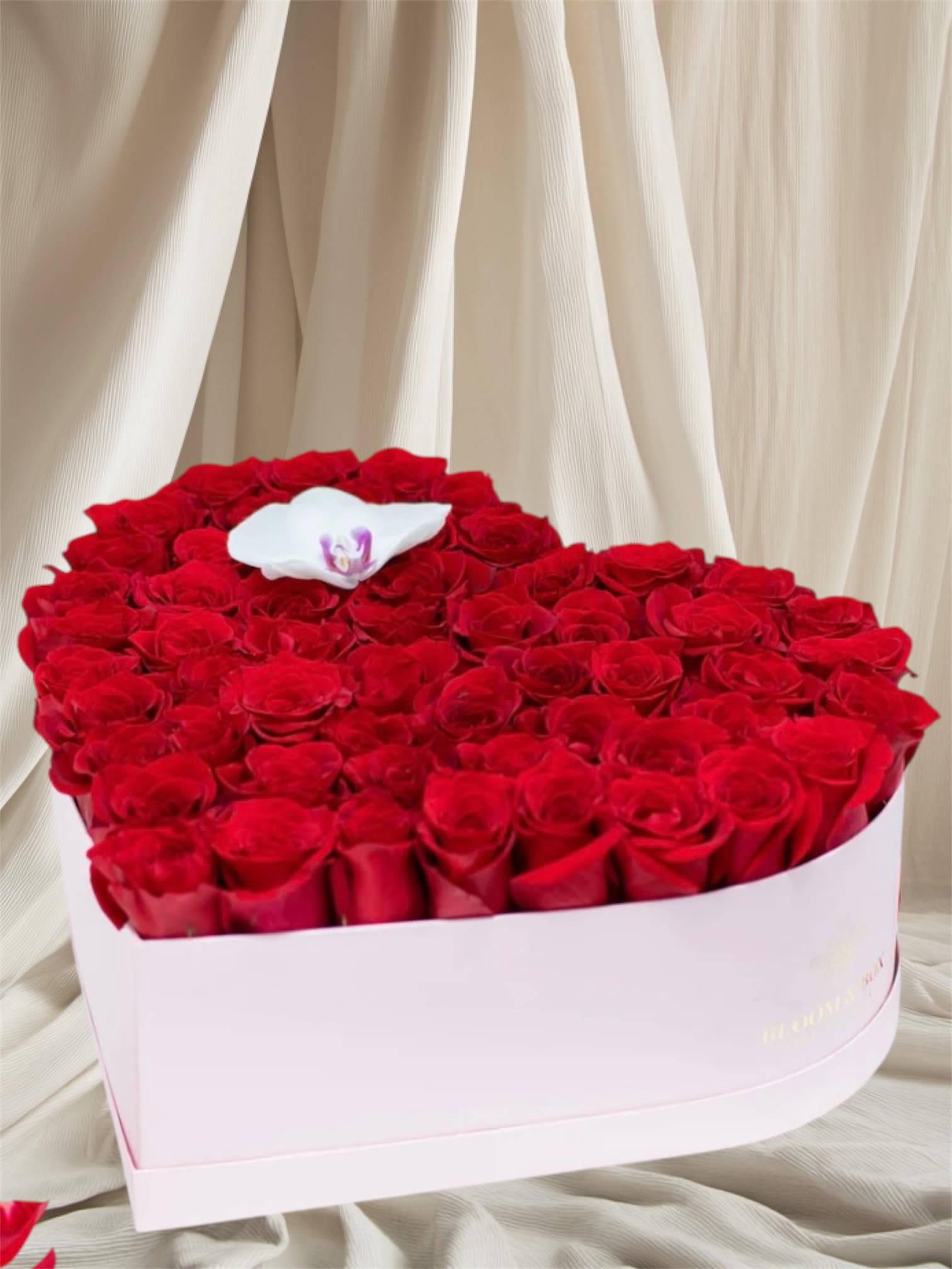 Heart-shaped box of red roses with a white orchid on top