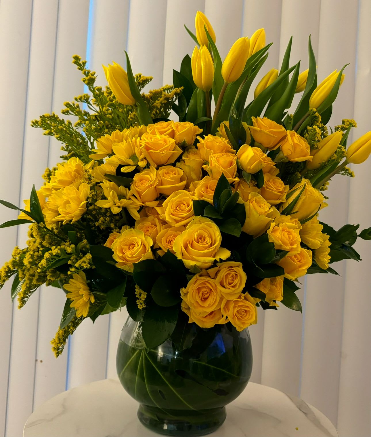 Yellow roses and tulips arranged in a glass vase