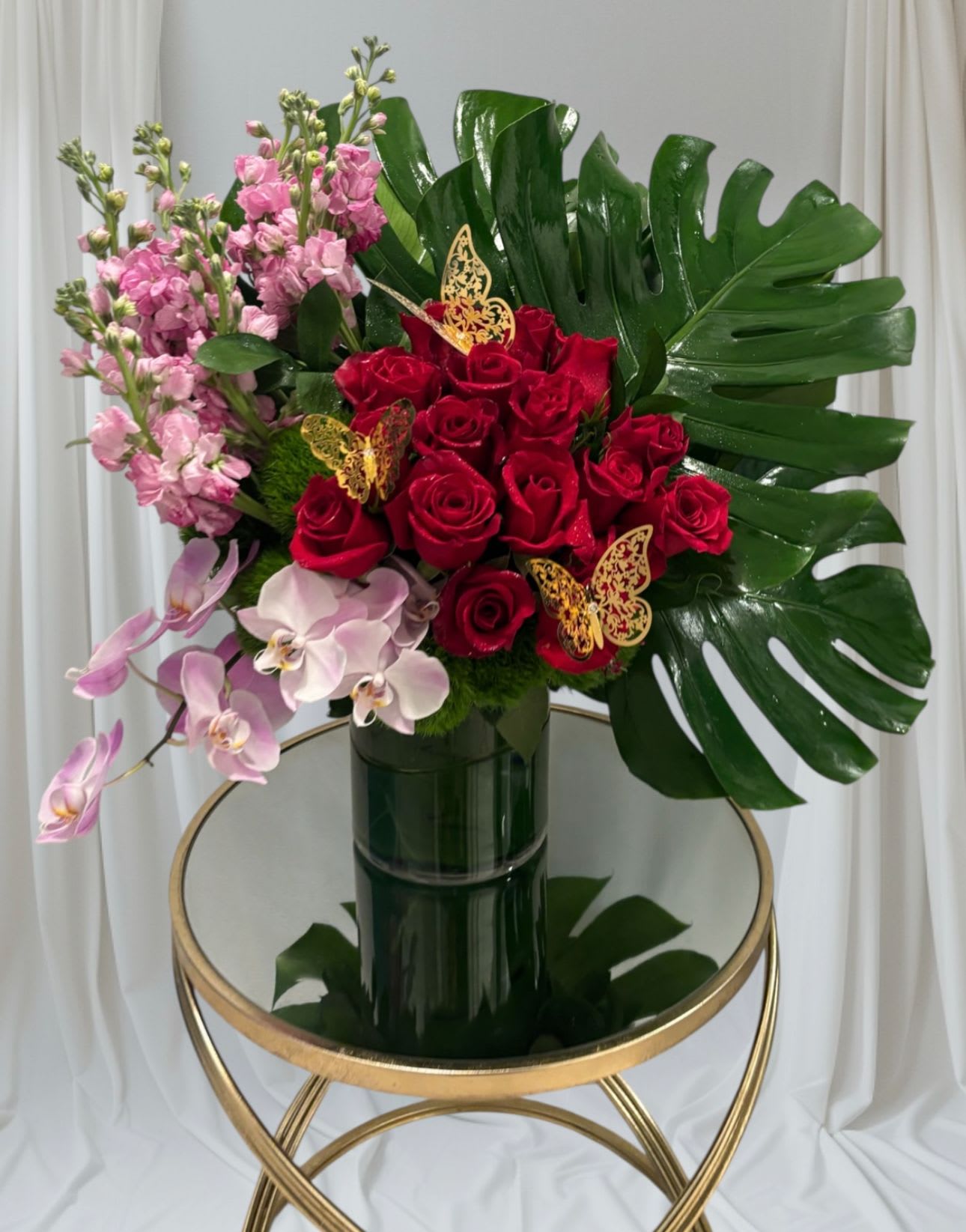 Bouquet of red roses, pink orchids, and pink stock in a dark vase