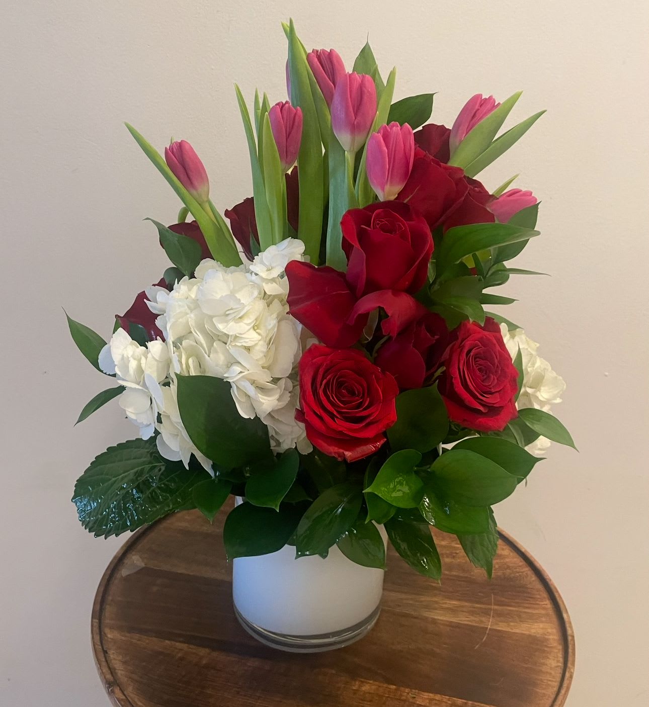 Bouquet of red roses, pink tulips, and white hydrangeas in a white vase