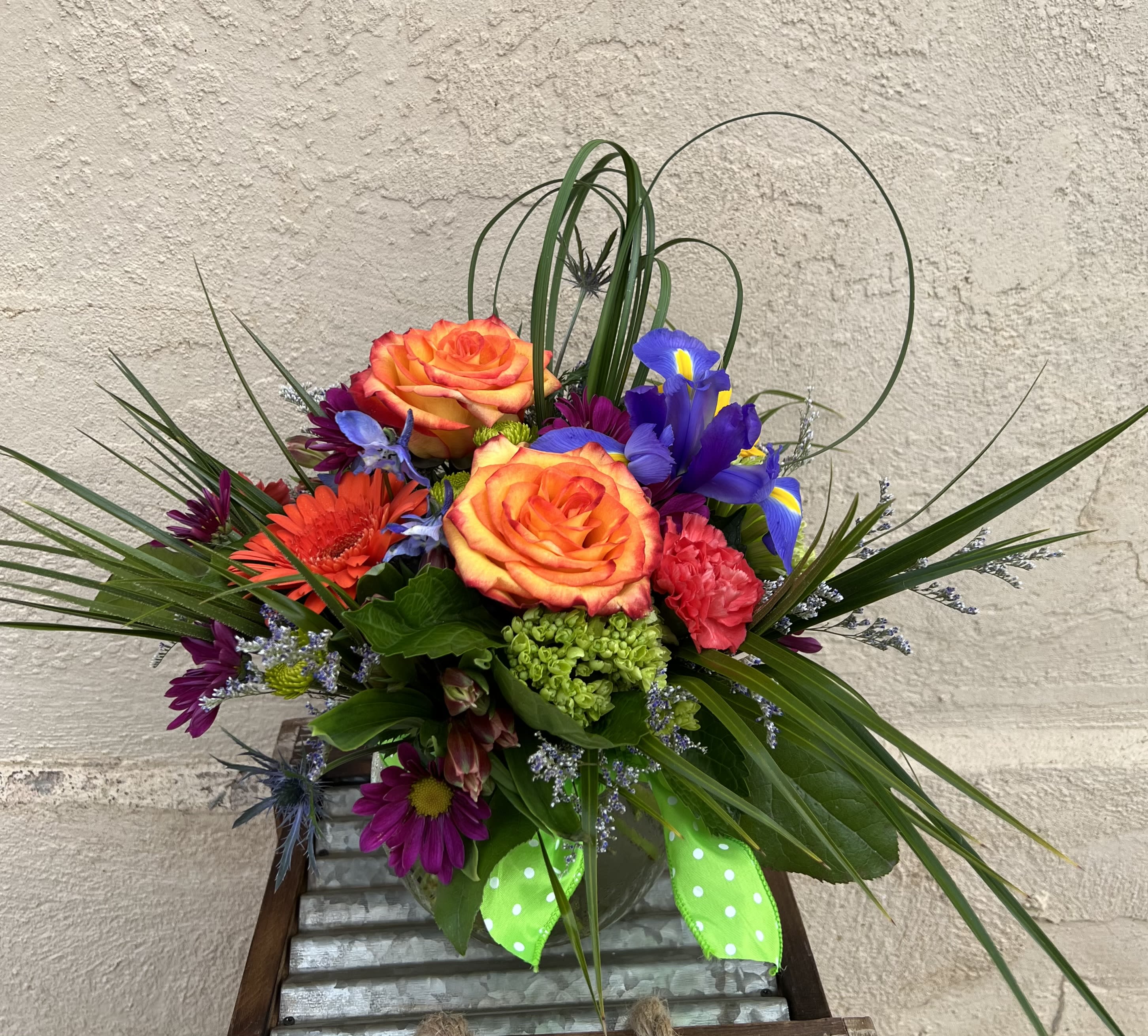 Colorful bouquet with orange roses, purple irises, and a green ribbon in a vase