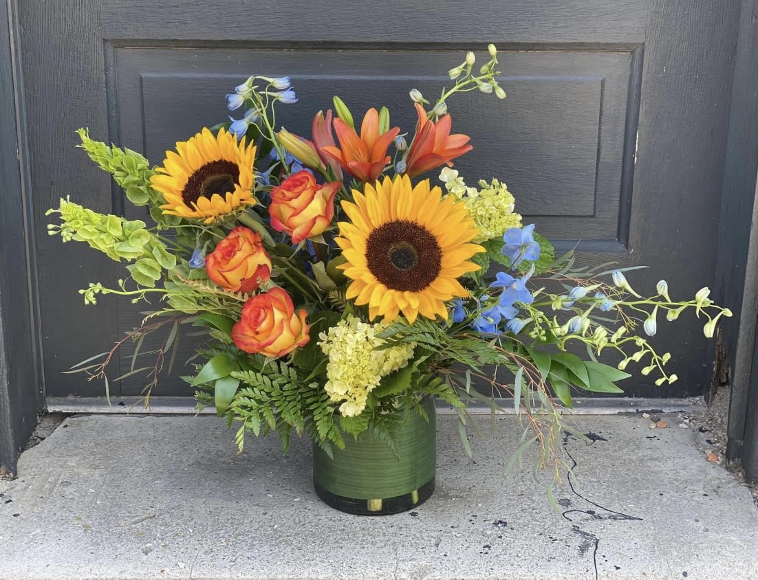 Mixed bouquet with sunflowers, roses, lilies, and blue flowers in a green vase