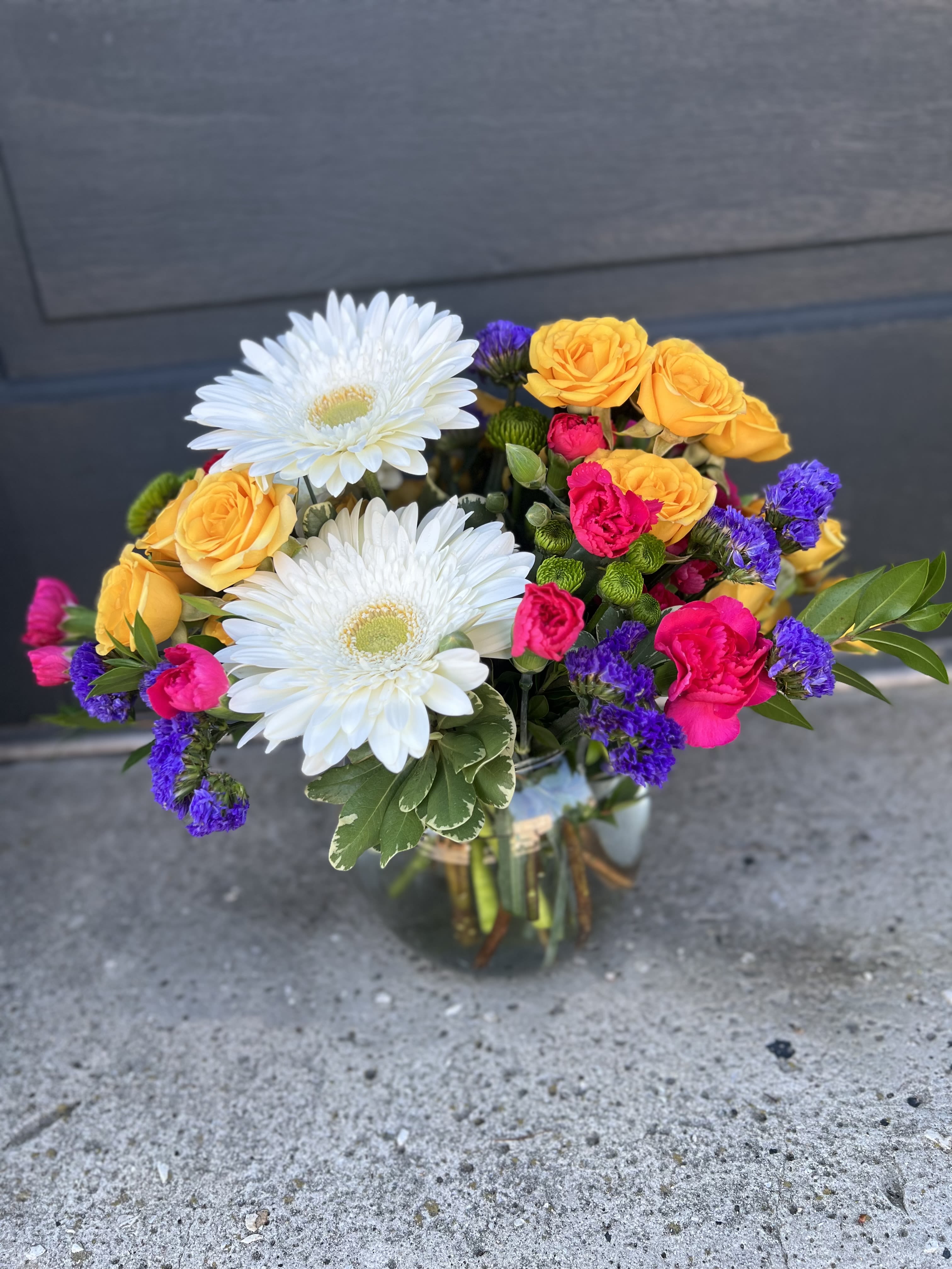 Mixed bouquet of white daisies, yellow roses, and pink blooms in a glass vase