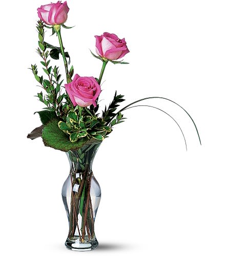 Three pink roses in a clear glass vase with greenery