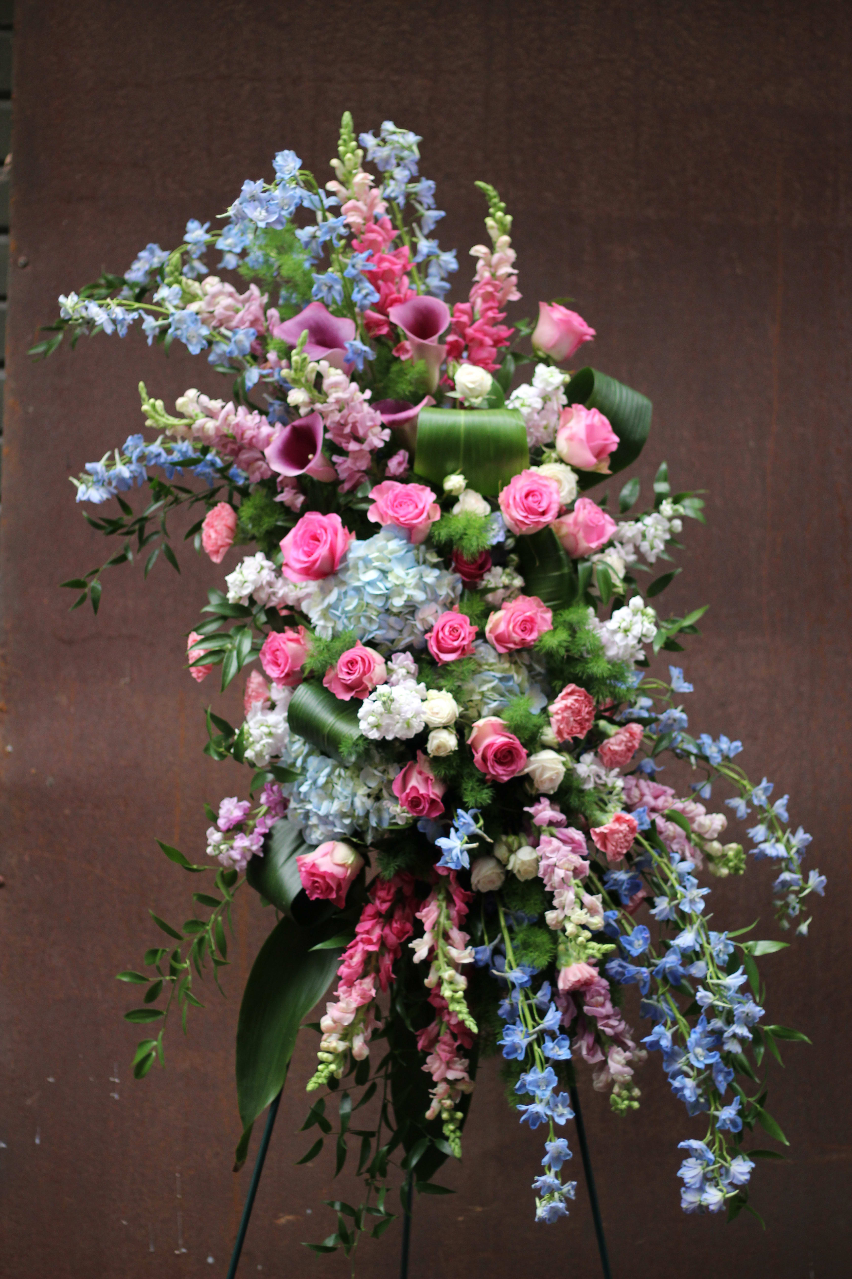 Tall floral standing spray with pink roses, blue delphinium, and purple calla lilies