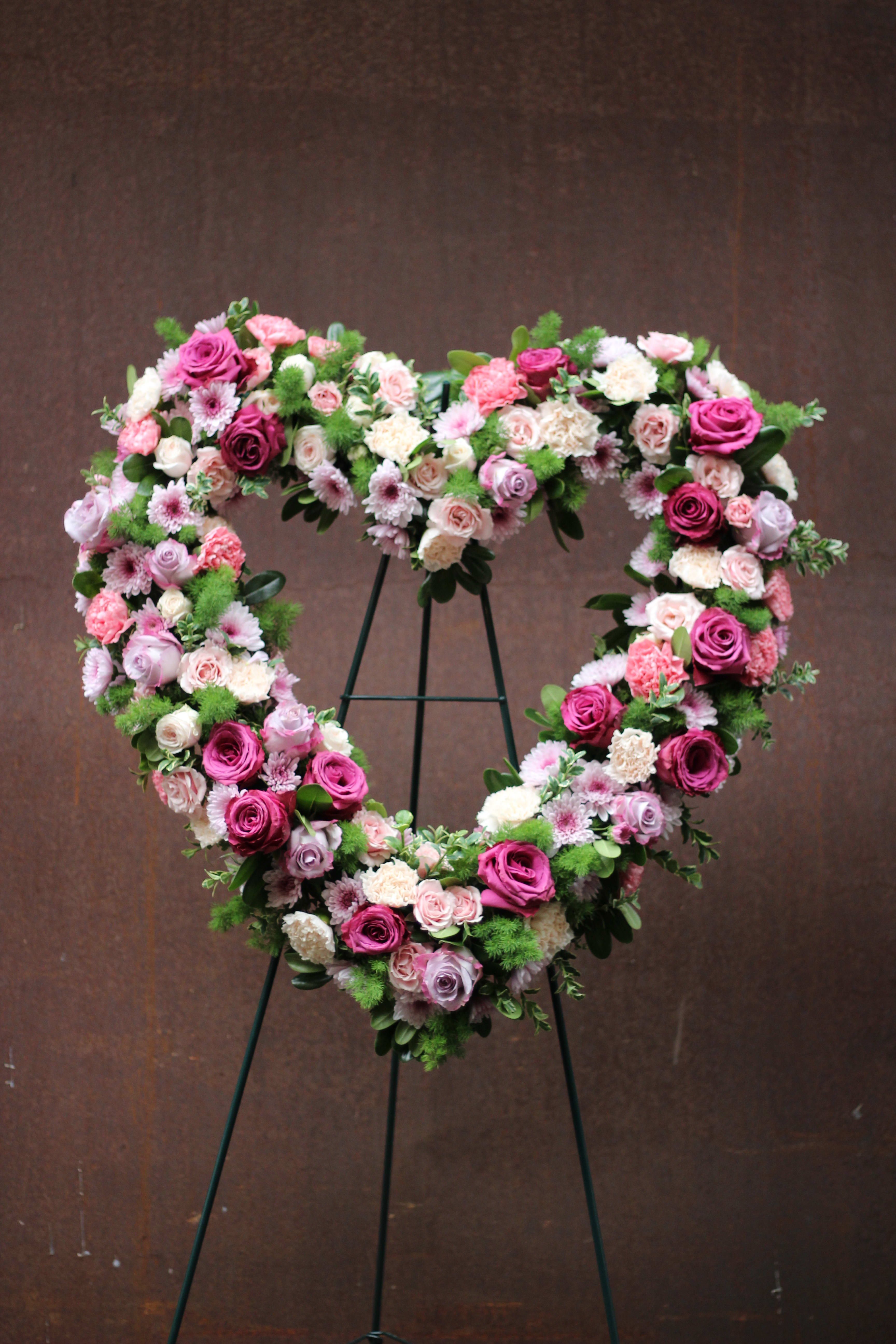 Heart-shaped floral wreath on a stand with pink and white roses