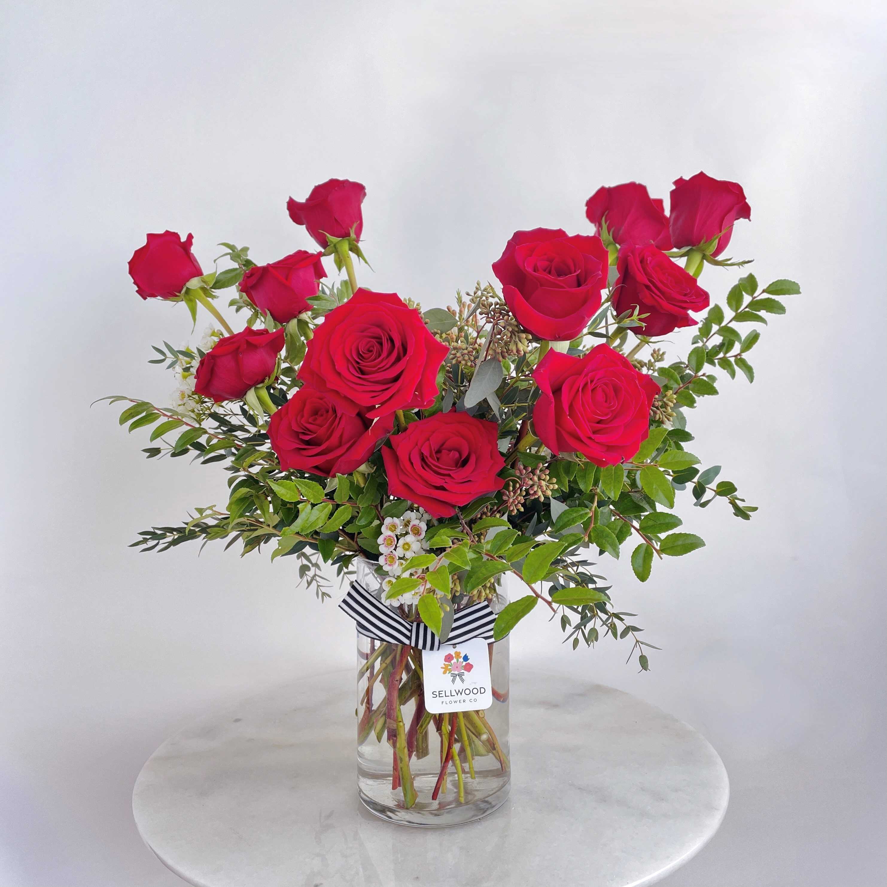 Red roses arranged in a clear glass vase with greenery