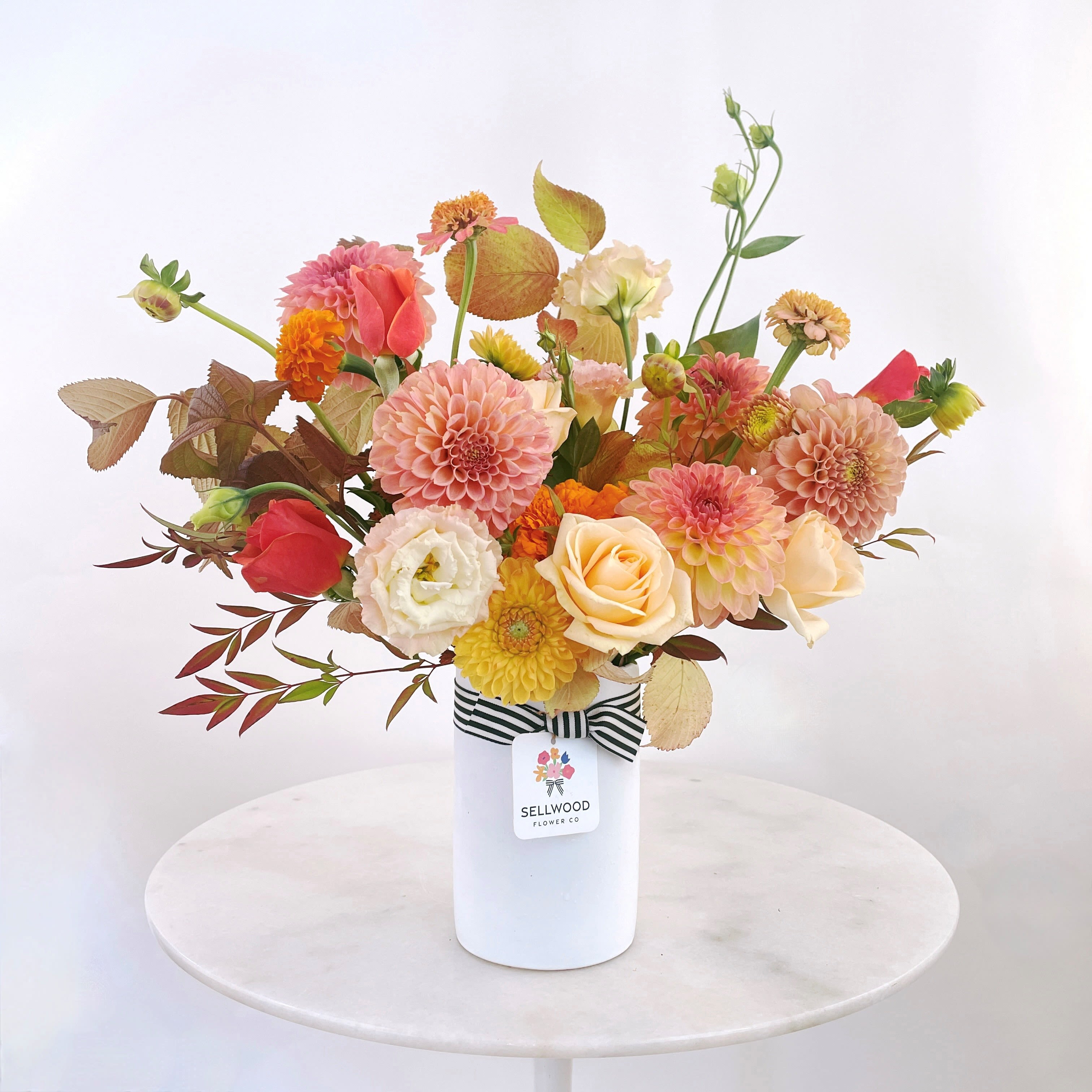 Mixed bouquet of peach, pink, and yellow flowers in a white vase