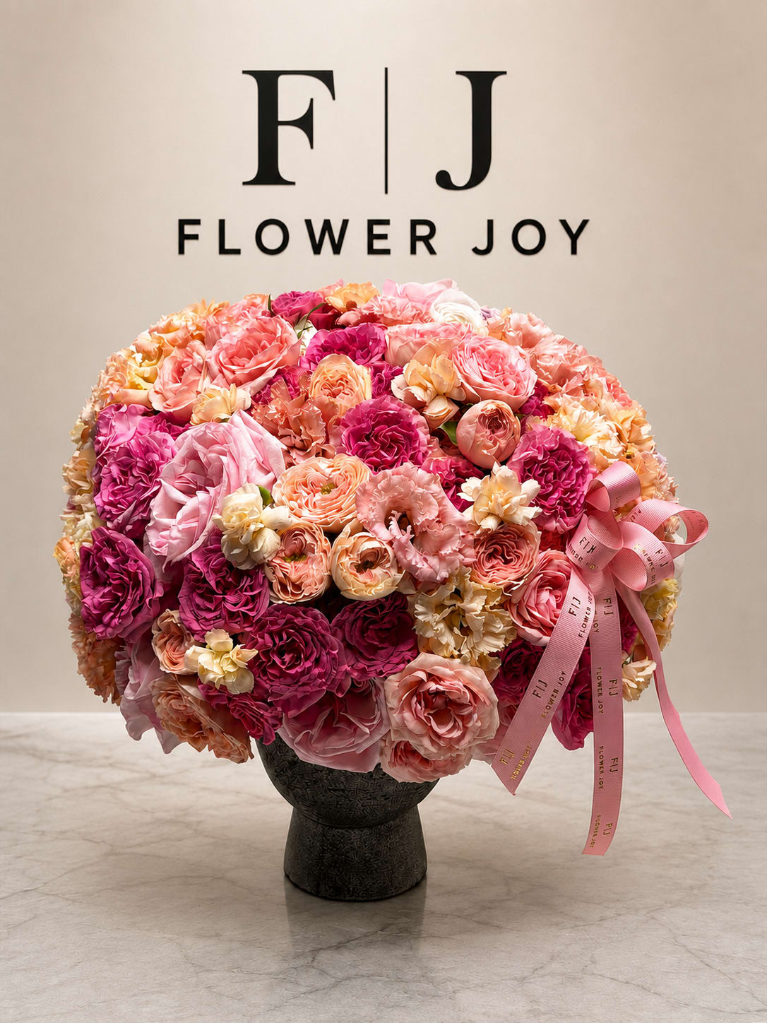 Large pink and peach flower arrangement in a dark vase with ribbon