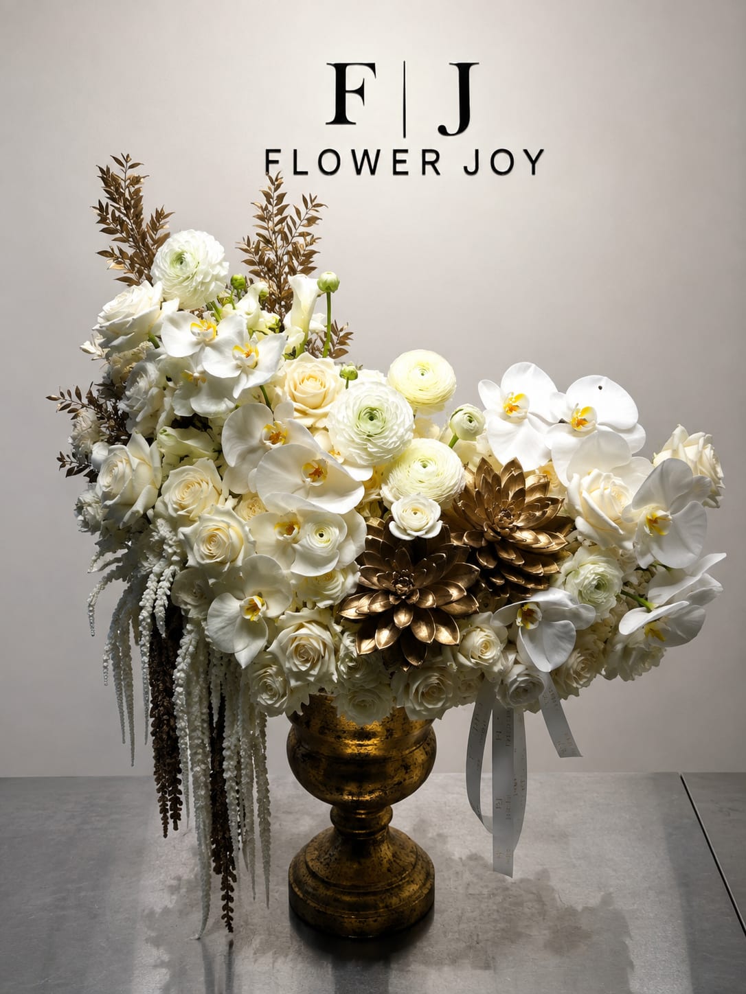 White floral arrangement in a gold urn with ribbon accents