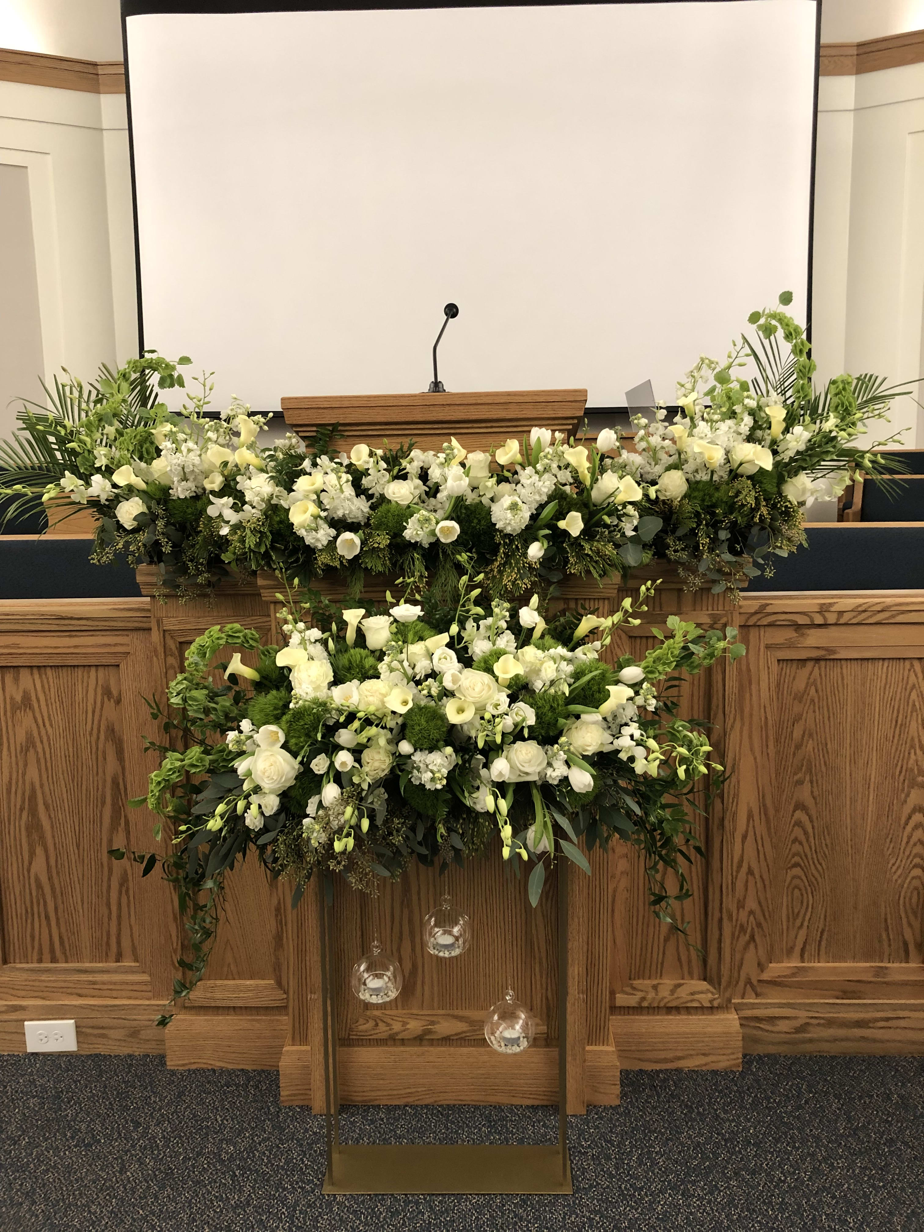 Large white floral arrangement on a podium with hanging glass ornaments