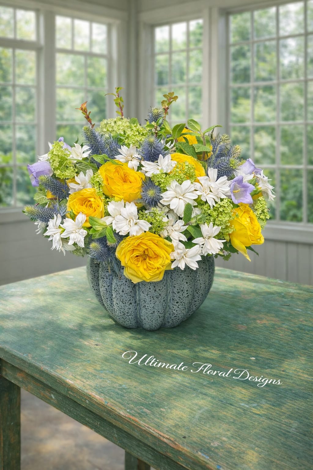 Golden Garden Radiance - Sunlit yellow garden roses take center stage in this bright floral bouquet, making it an ideal birthday bouquet, get-well gift, or cheerful housewarming arrangement. The Golden Garden Radiance is designed to make the person you're thinking of feel uplifted and genuinely seen-warm golden tones balanced with cool blue accents create a joyful, celebratory impression perfect for everyday gifting or sending thanks.  White blooms and viburnum surround the roses for a fresh, garden-picked look, while spiky blue thistle and soft lavender bell-shaped campanula add unexpected texture and cool contrast. The flowers are gathered in a rounded, gray-blue ceramic vase with a pumpkin-like ribbed form that gives the design a slightly rustic, seasonal character and a pleasing tactile presence on tabletops or entryway consoles.  Sized to sit comfortably on a small table, this light, airy arrangement arrives ready to display; simple care-fresh water and a cool spot away from direct heat-keeps it is looking its best. Same-day delivery is available in Great Falls, McLean, Vienna, Reston, Arlington, and Washington, DC, so you can send an immediate, heartfelt surprise that brightens someone's day.