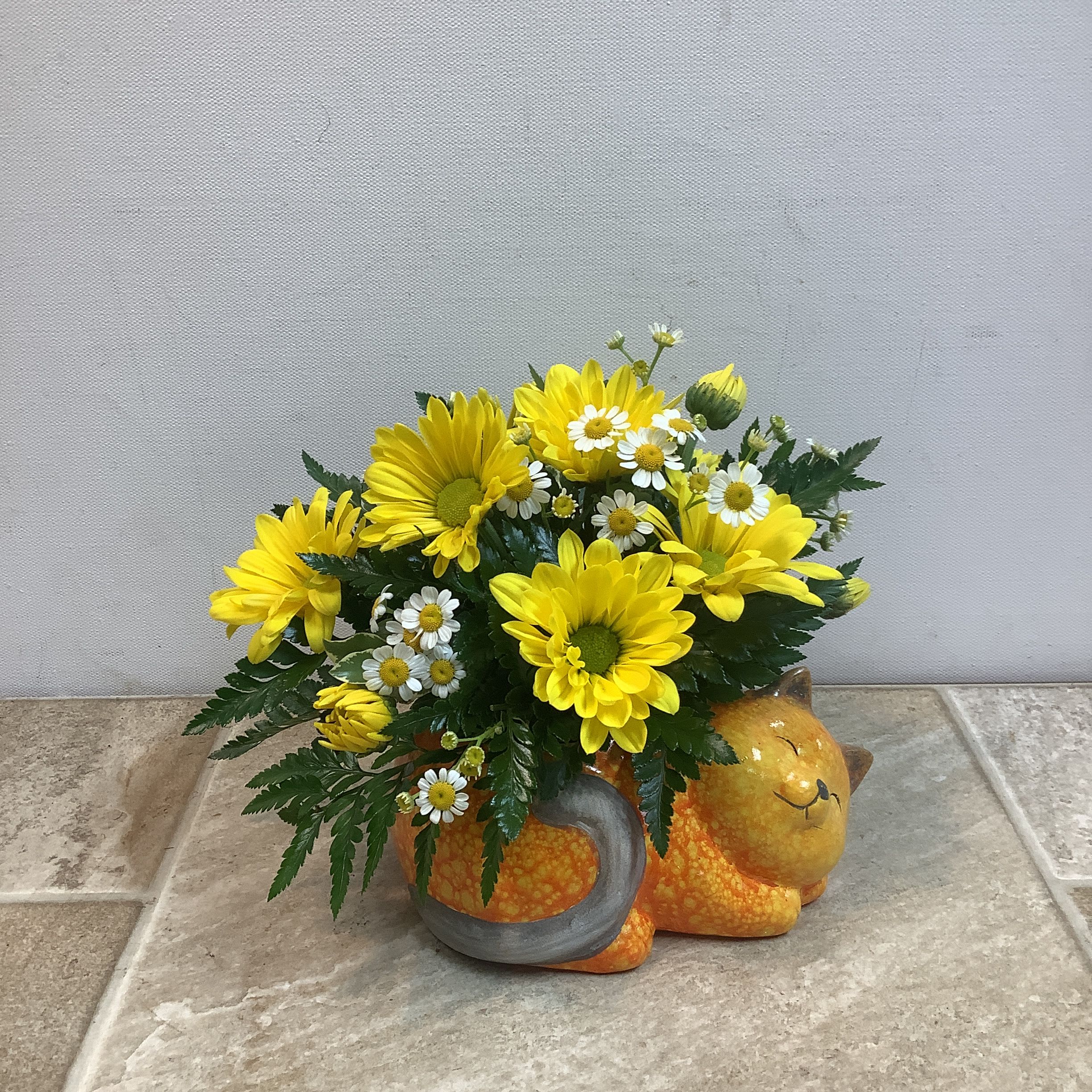 Yellow daisies and white daisies arranged in a cat-shaped ceramic container