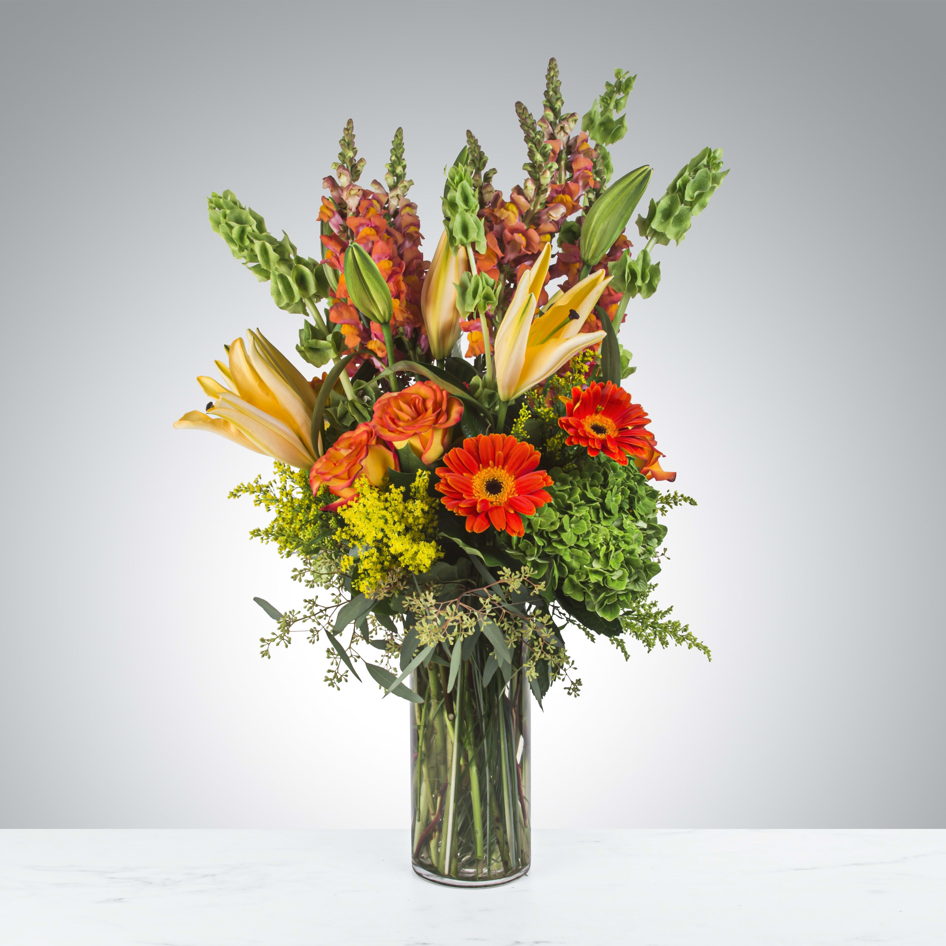Tall bouquet of orange and yellow flowers in a clear glass vase
