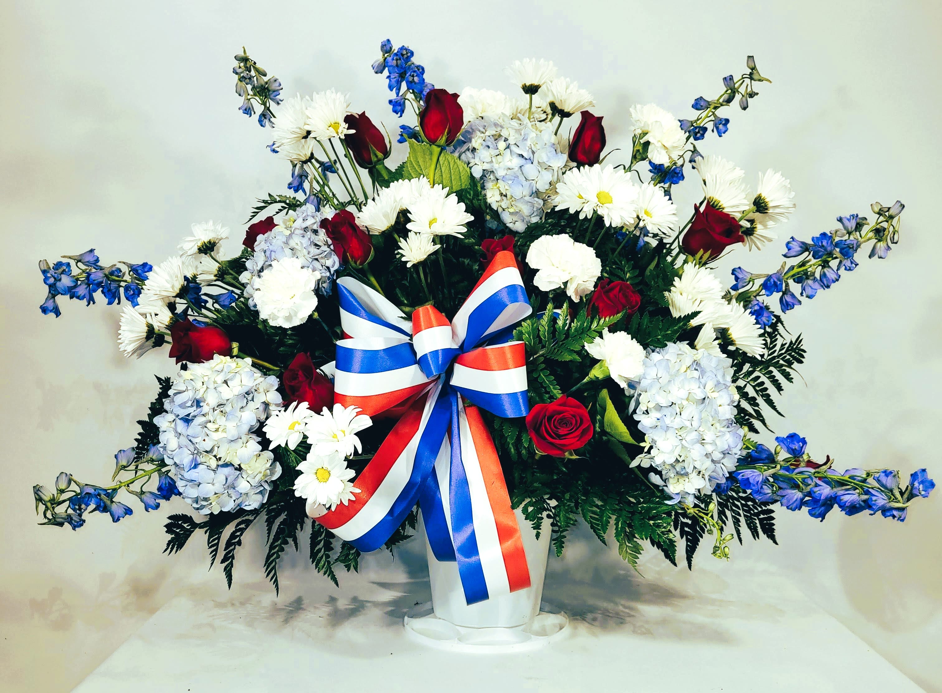 Large red, white, and blue floral arrangement in a white vase with a ribbon bow