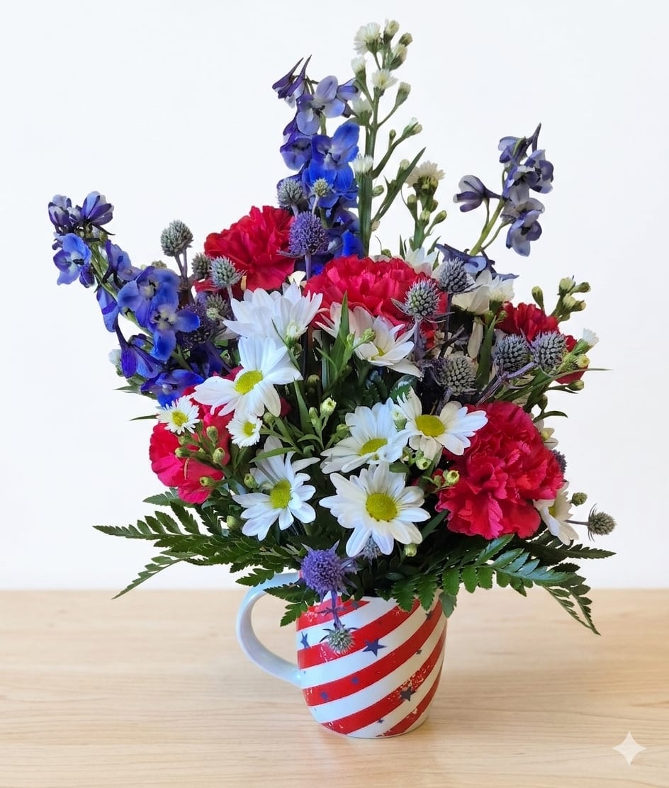 Red, White and Brew Mug  - Bright red carnations, crisp white daisies, and vivid blue delphinium are arranged upright in a compact, festive presentation-perfect as a patriotic flower arrangement for summer holidays, Memorial Day, or to celebrate an event with red, white, and blue flair. The small daisy blooms soften the texture while the saturated colors deliver a cheerful, celebratory impression that will make the person you're thinking of feel honored and brightened.  This mixed-color bouquet sits in a reusable ceramic mug decorated with red-and-white stripes and stars, giving it a casual, giftable vibe. Approximately 12" tall, the arrangement also includes white monte casino and other seasonal filler to round out the composition and add lightness between the larger blooms.  Send this mug arrangement to someone who enjoys easy-care, display-ready flowers-a neighbor, teacher, veteran, or host-so they can set it on a counter or desk and enjoy the patriotic pop of color. The ceramic mug is reusable, making this both a keepsake and a cheerful floral gift.
