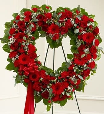 Heart-shaped red floral wreath on a stand with a red ribbon