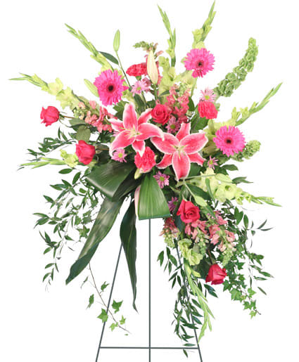 GRATEFUL HEART SPRAY - Honor a lost loved one with the Grateful Heart standing spray. This spray is ideal for encompassing a lively spirit and would be a beautiful addition to any funeral service, memorial service, or wake. It features vibrant Stargazer lilies, Gerbera daisies, and roses in beautiful hues of pink that stand out against the luscious sea of aspidistra, giving comfort to grieving hearts. 