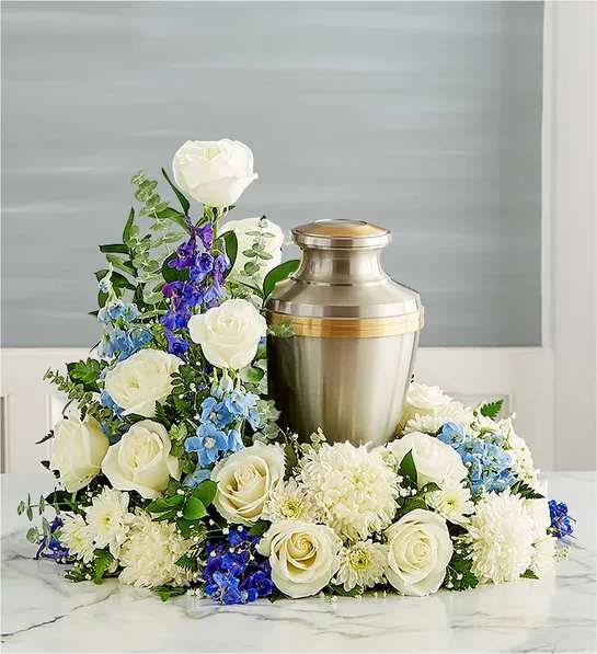 Cremation Wreath- Blue and White - Honor their memory and celebrate the joy they brought to their loved ones. Our elegant wreath arrangement is handcrafted from a soothing mix of blooms, creating a peaceful tribute, while offering comfort during a difficult time..All-around asymmetrical wreath arrangement of white roses, football mums and cushion poms, blue delphinium; accented with baby’s breath and assorted greenery