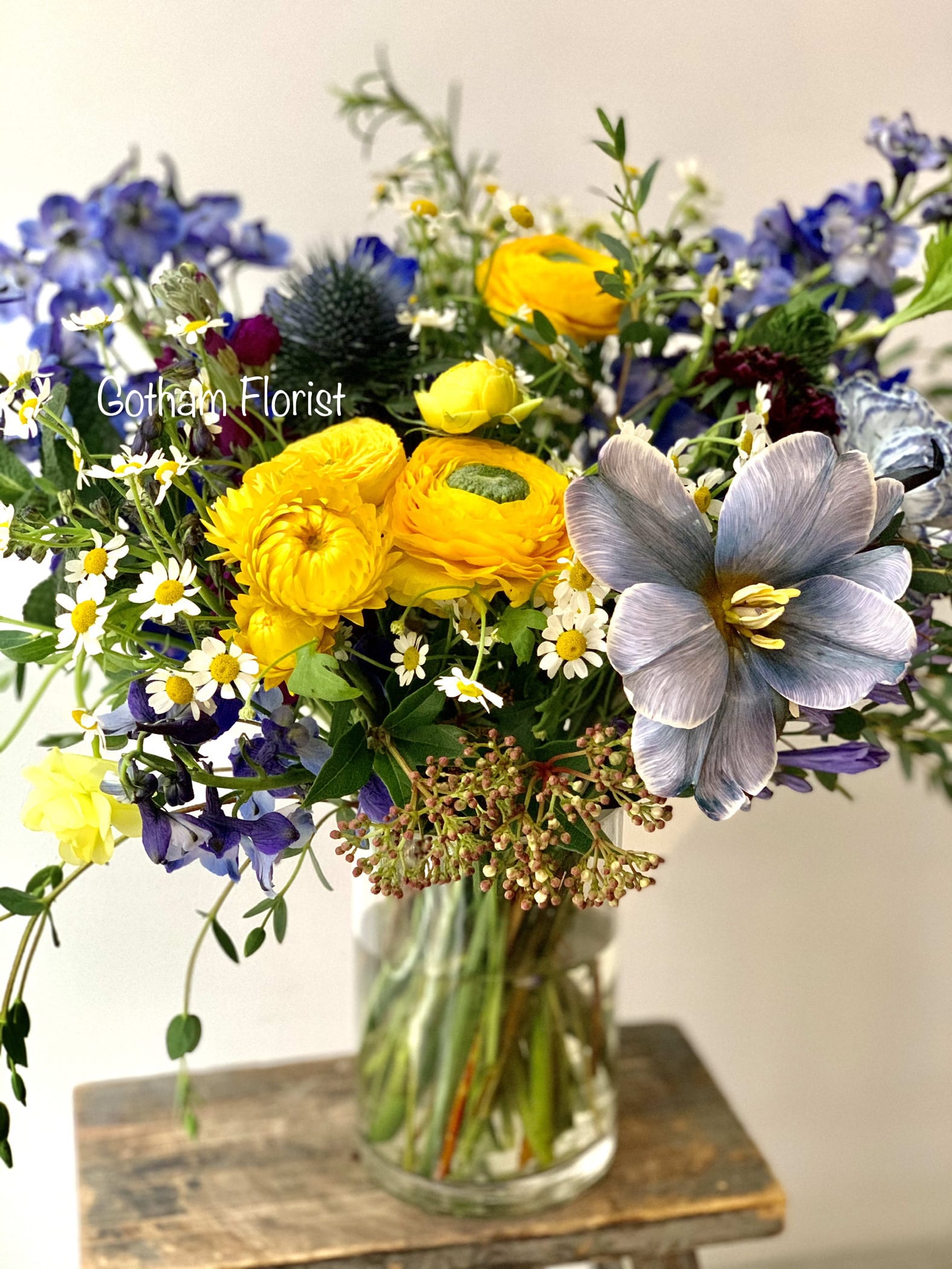 Mixed bouquet in a clear glass vase with yellow, blue, and white flowers