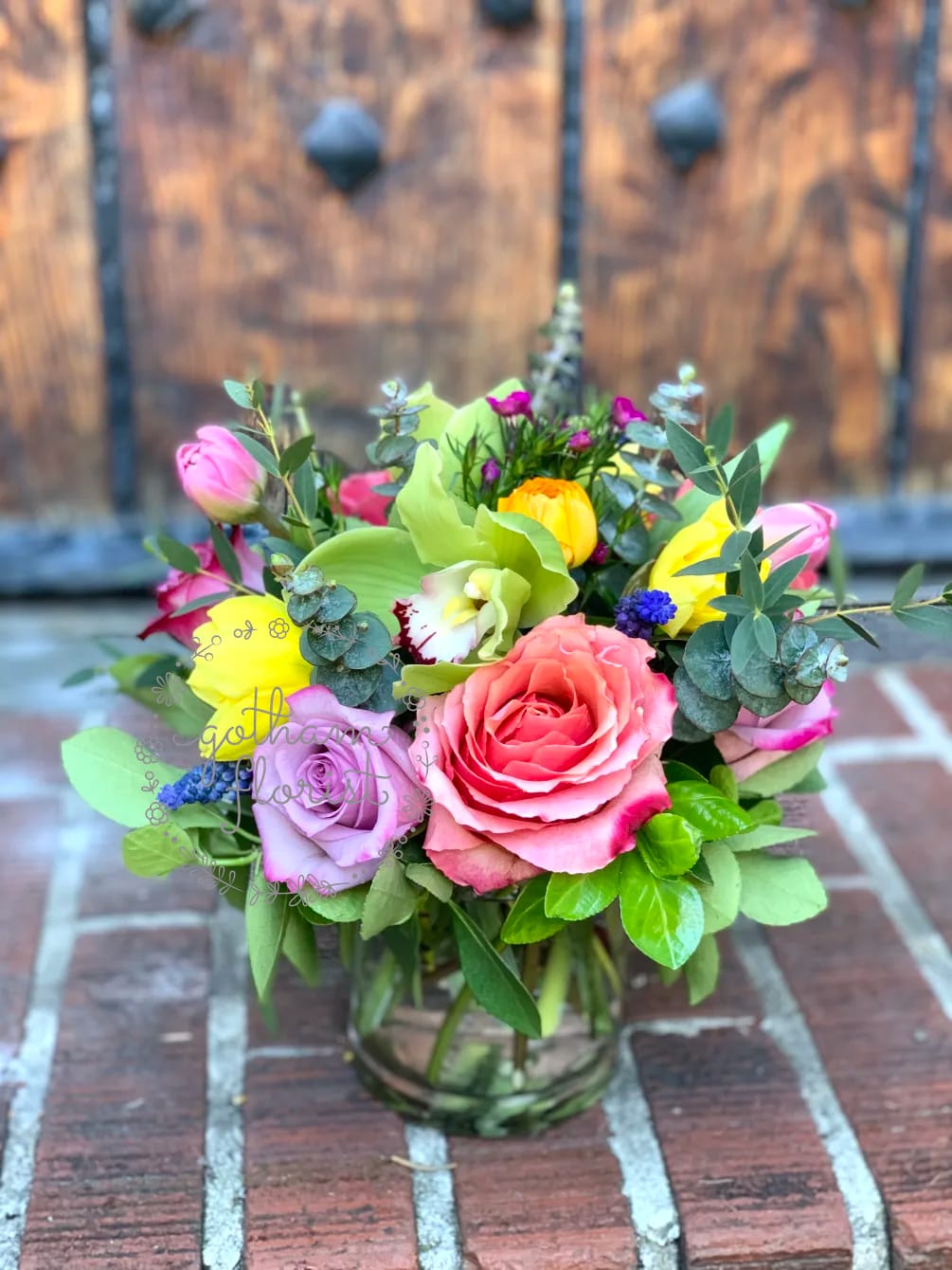 Colorful mixed bouquet of roses, tulips, orchids, and ranunculus in a clear glass vase