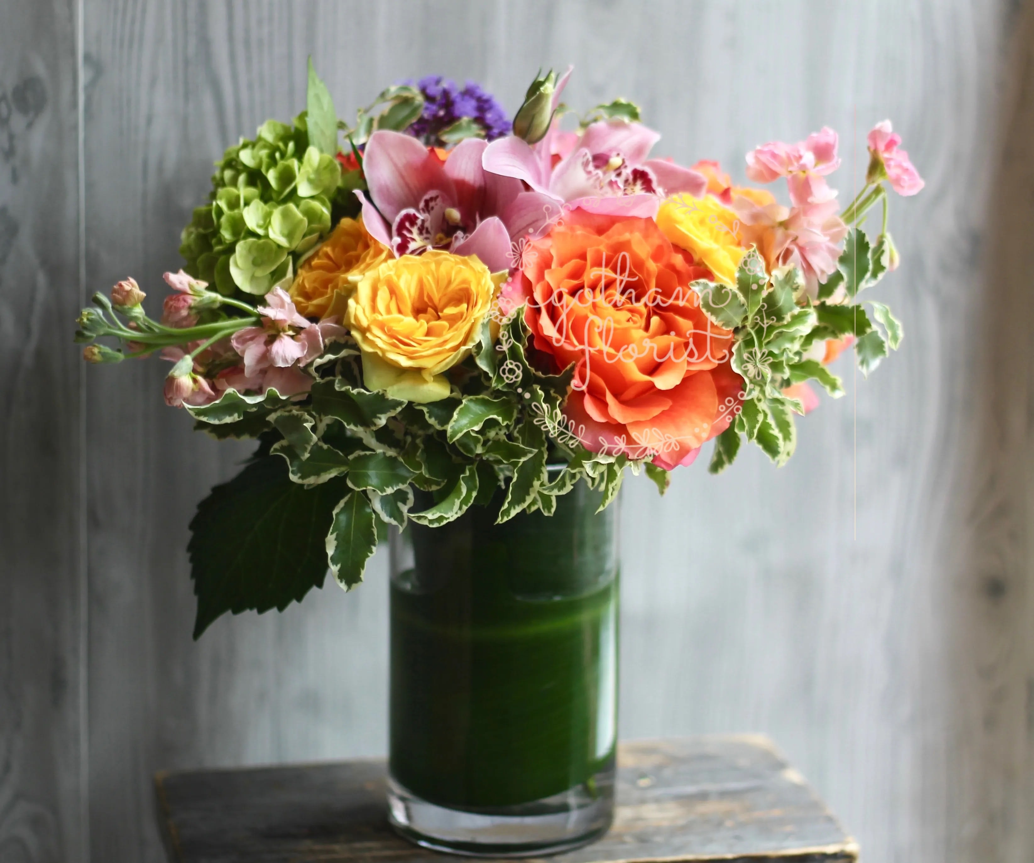 Mixed bouquet in a green glass vase with pink, orange, and yellow blooms