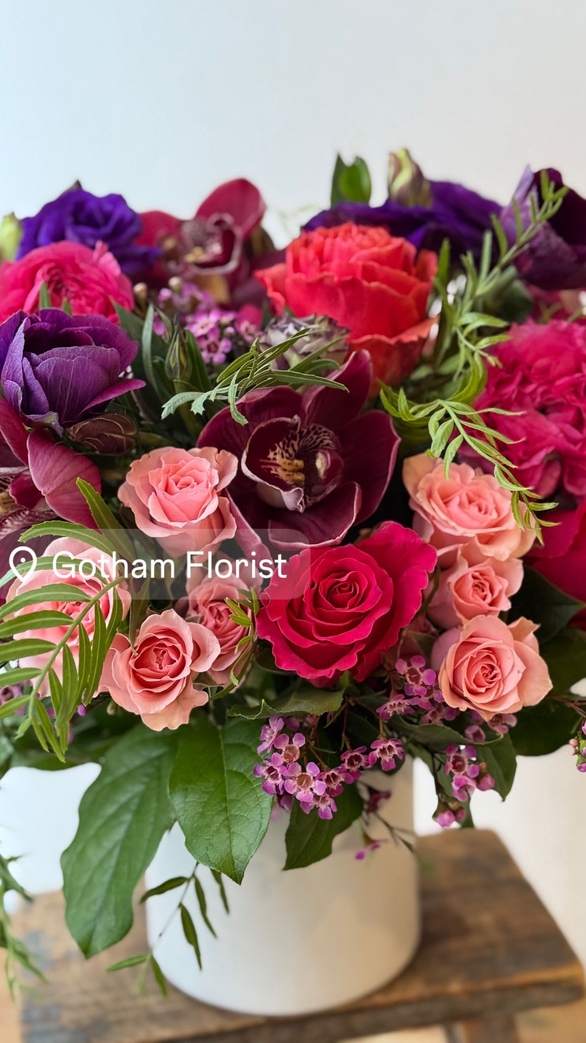 Mixed bouquet of pink, purple, and red flowers in a white vase