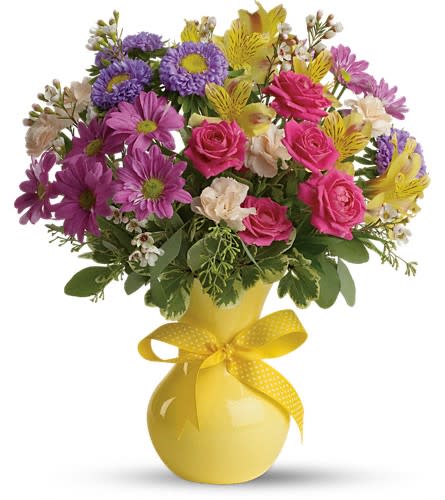 Mixed bouquet of pink, purple, and yellow flowers in a yellow vase with a ribbon