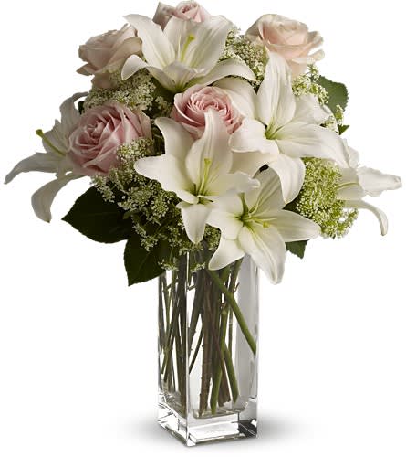 White lilies and pale pink roses arranged in a clear glass vase