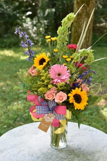 Mixed bouquet with sunflowers, pink gerberas, and roses in a glass vase