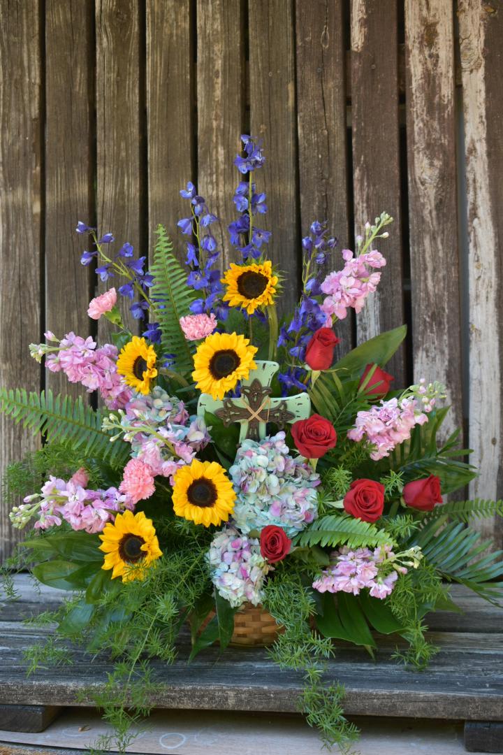 Colorful Funeral Basket - A grand and colorful funeral basket of pretty suns, stock, red roses, hydrangeas, delphinium, and carnations.