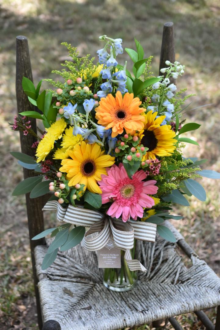 Mixed bouquet with gerbera daisies, sunflowers, and blue flowers in a glass vase