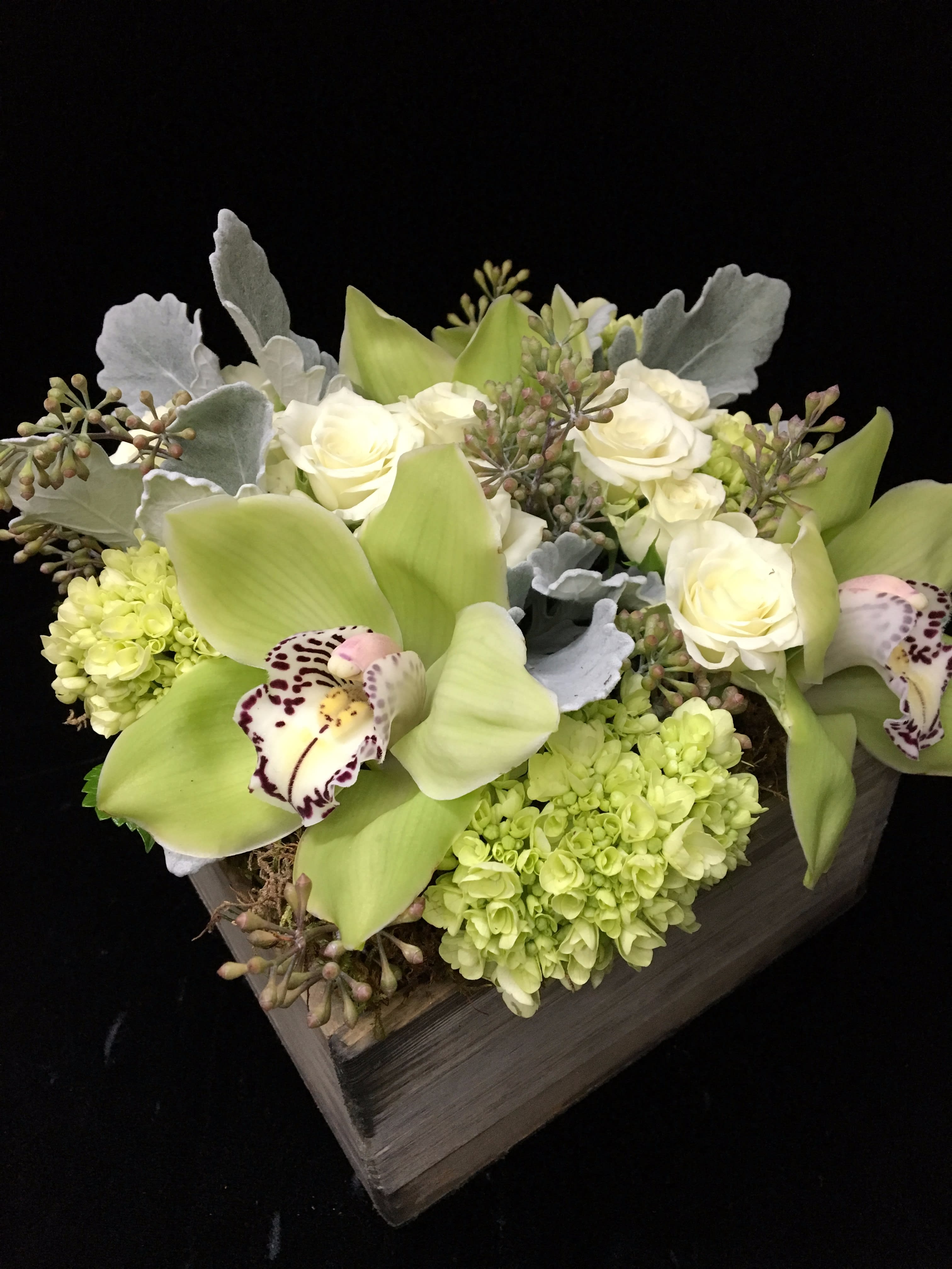 Low arrangement of green orchids, white roses, and hydrangeas in a wooden box.