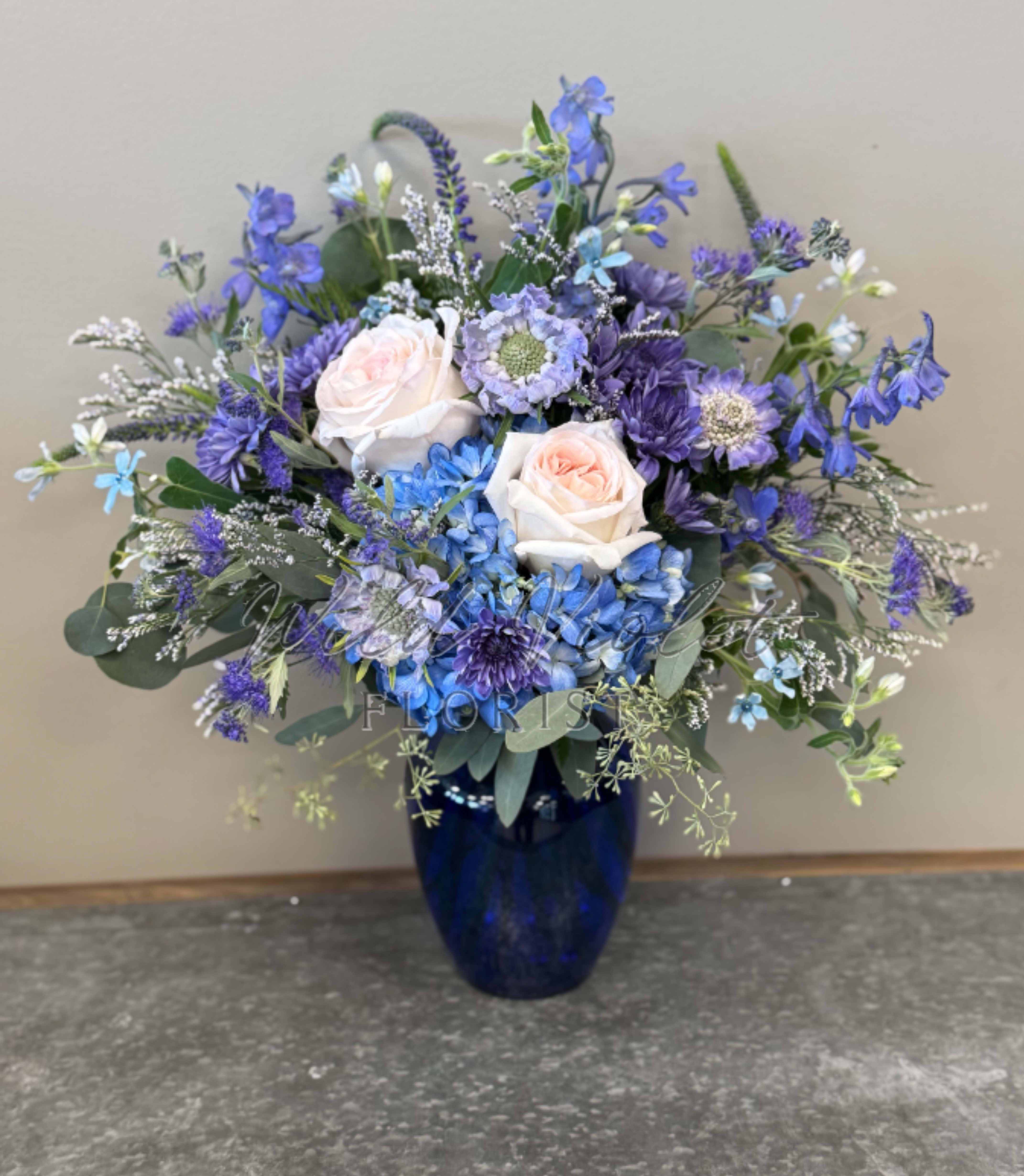 Blue and lavender floral arrangement in a dark blue vase