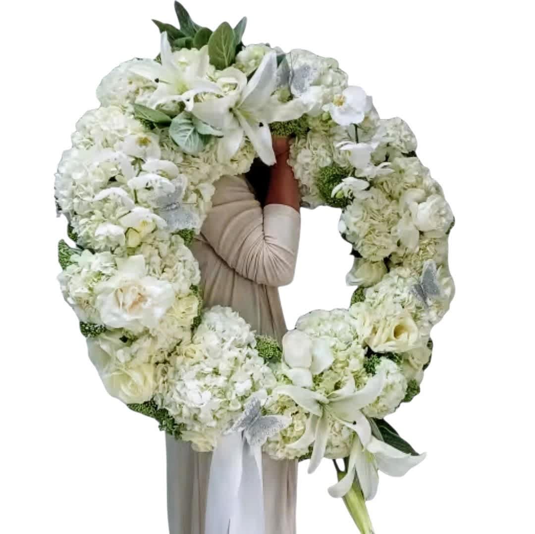Large white floral wreath with lilies and hydrangeas held by a person