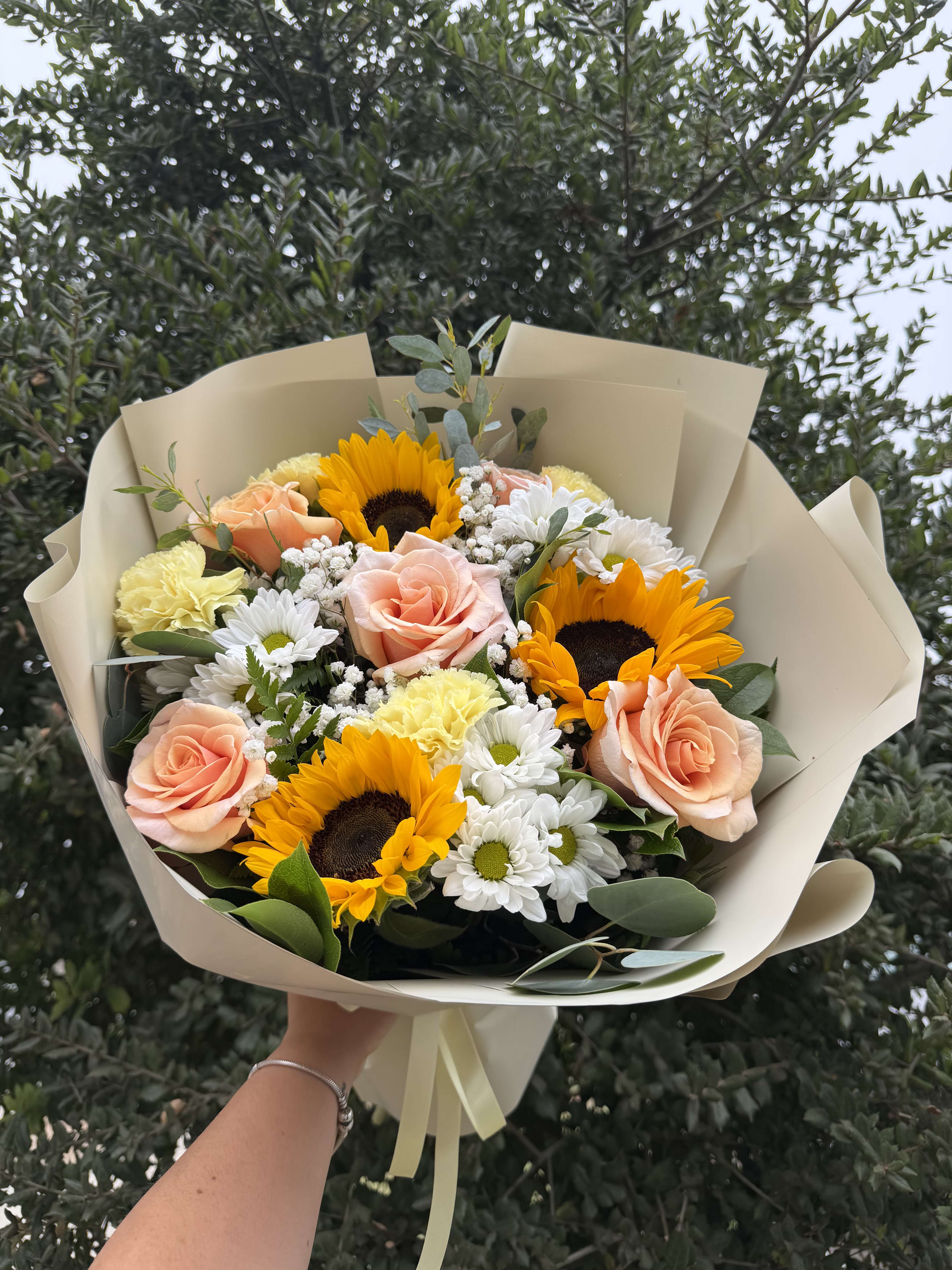 Bouquet of peach roses, sunflowers, and white daisies in beige wrap