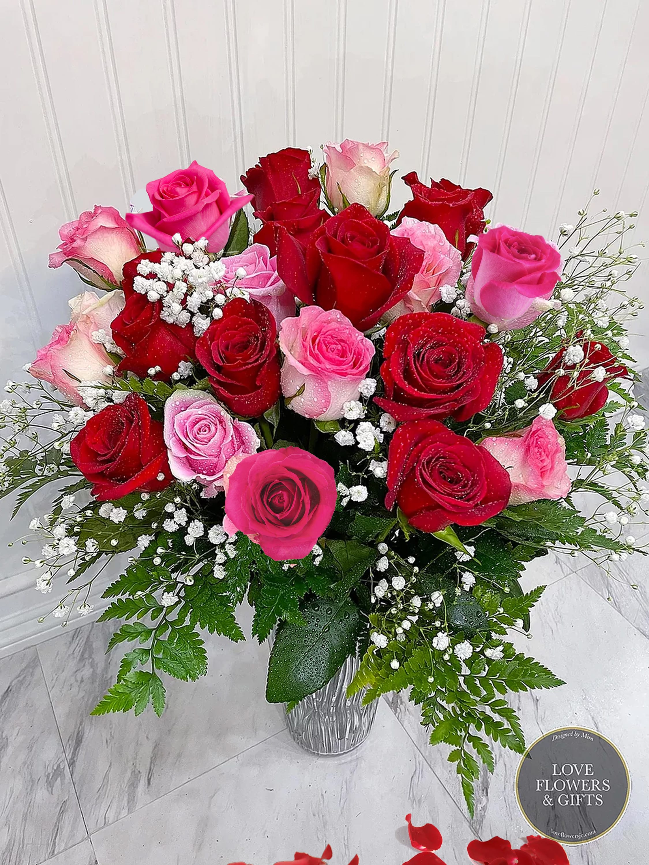 Arrangement of red and pink roses with white filler flowers in a textured glass vase