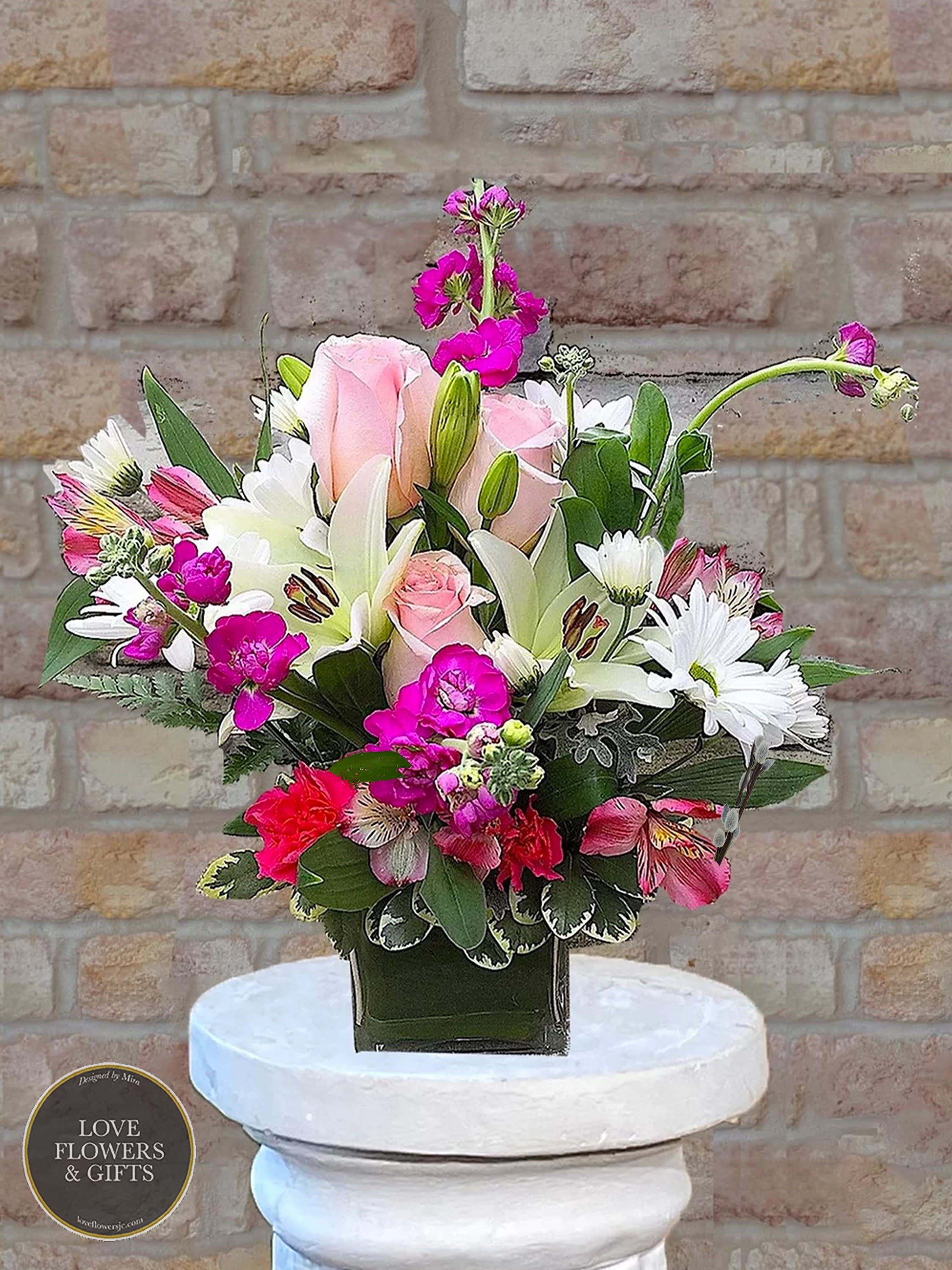Compact arrangement of pink roses, white lilies and bright pink blooms in a green glass cube vase
