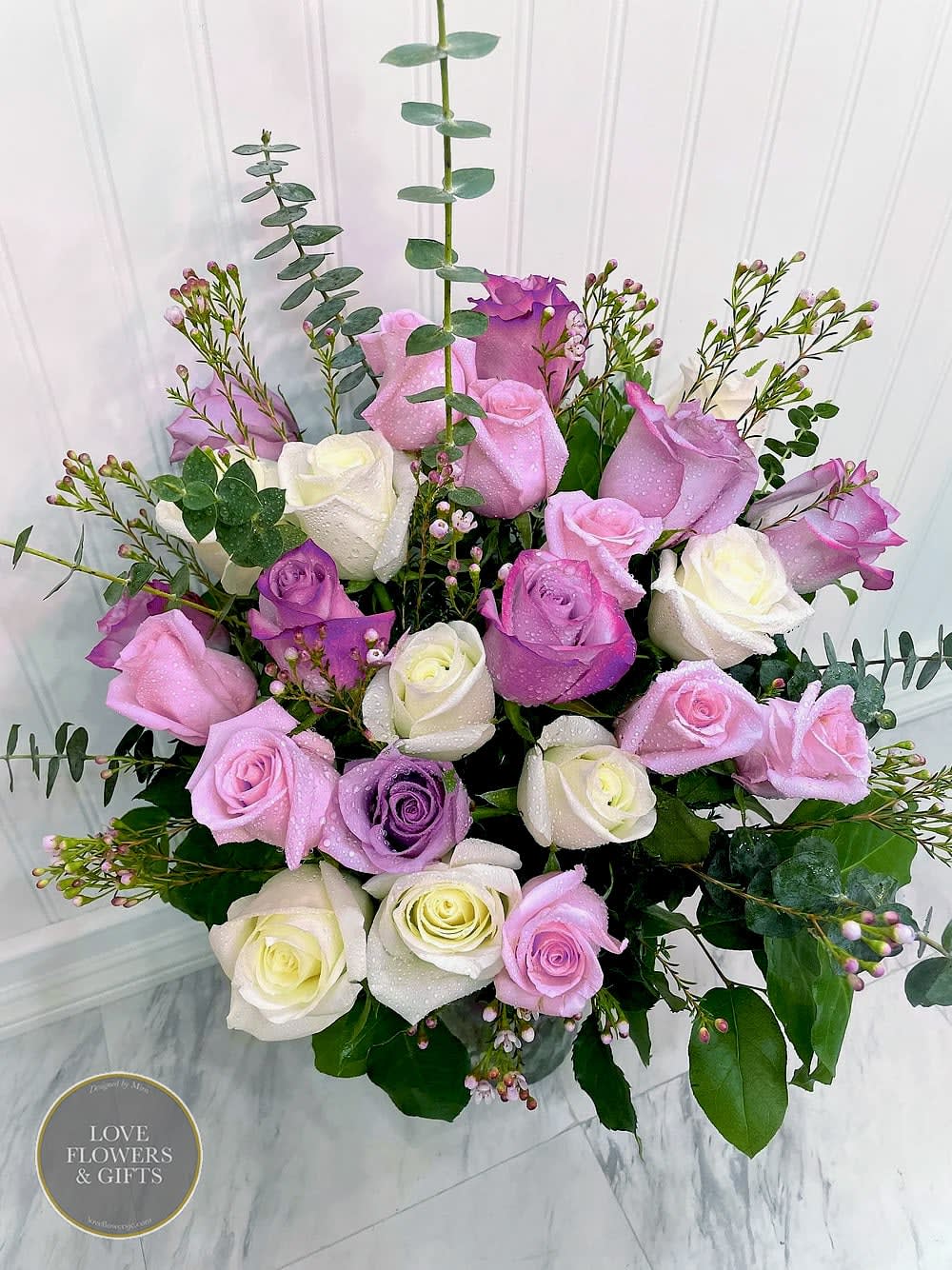 Pastel pink, lavender, and white roses arranged in a clear glass vase.