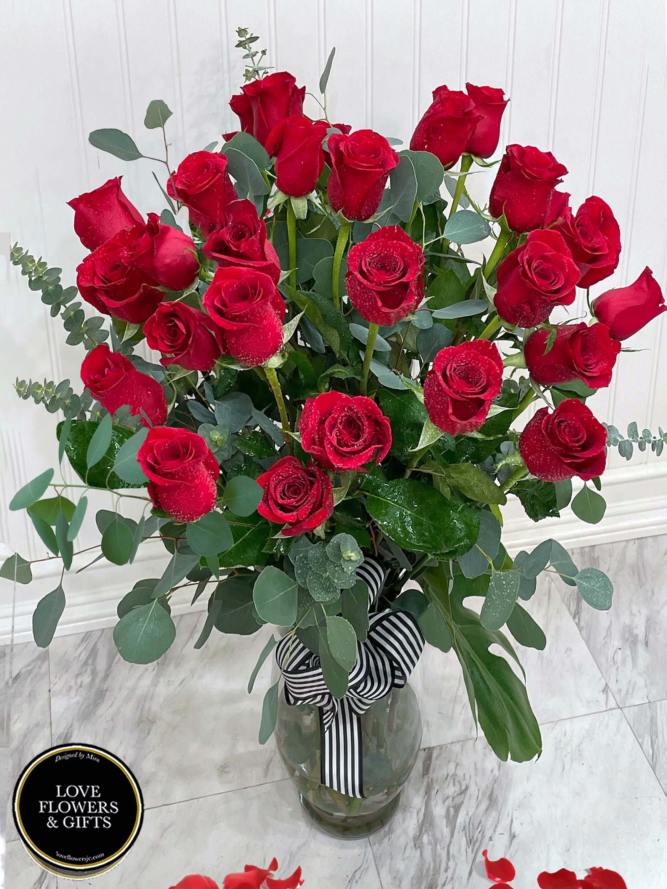 Tall arrangement of long-stemmed red roses in a clear glass vase with striped ribbon