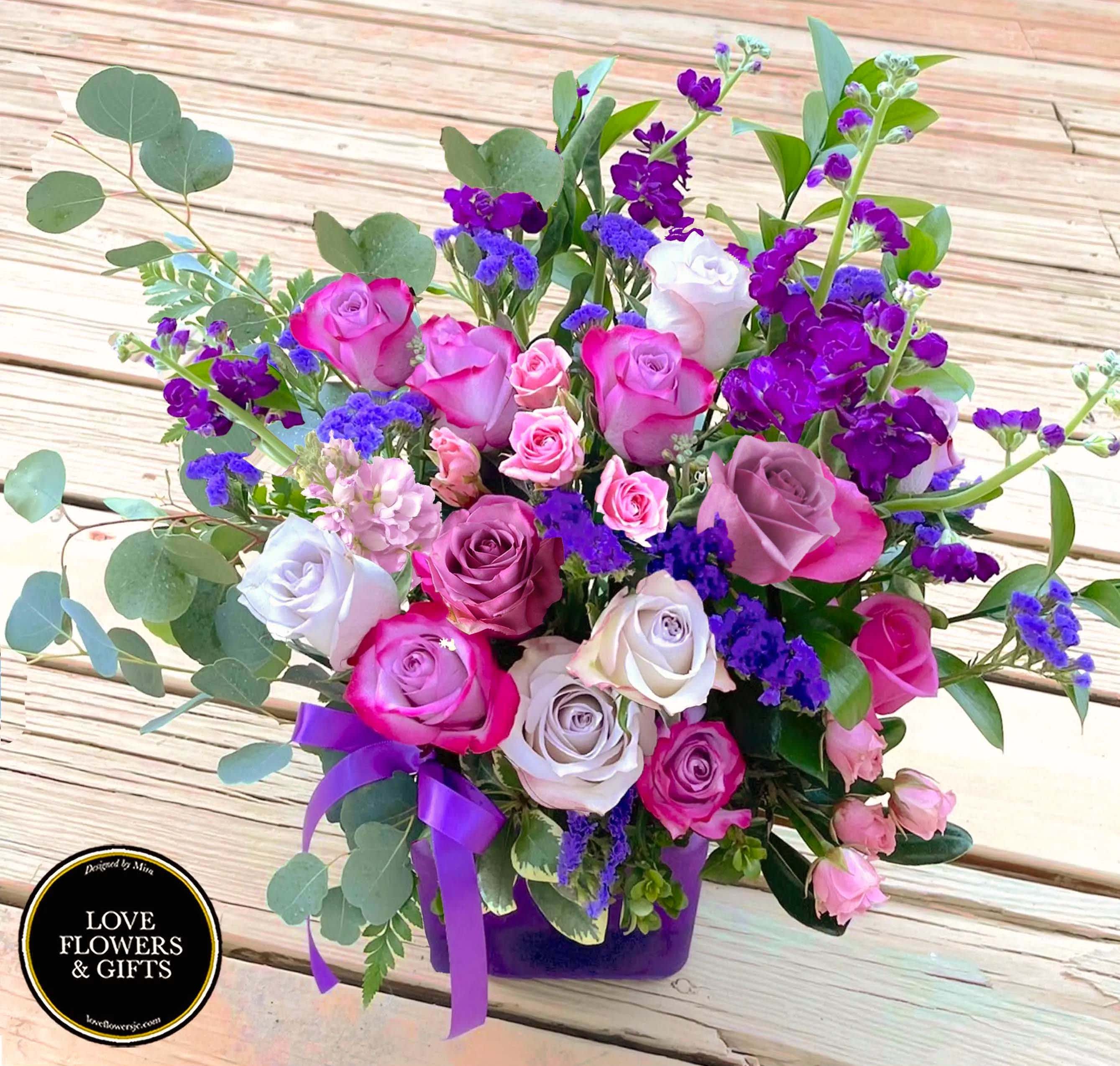 Mixed bouquet of pink and lavender roses with purple flowers in a purple vase