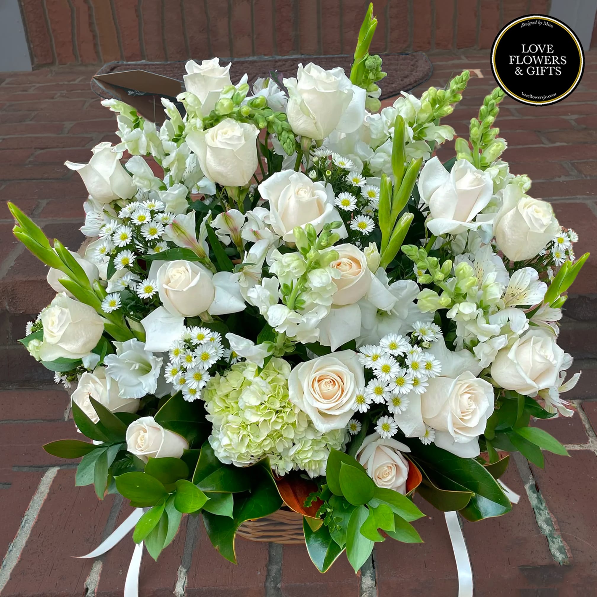 White and cream roses with small white daisies and hydrangea arranged in a basket.